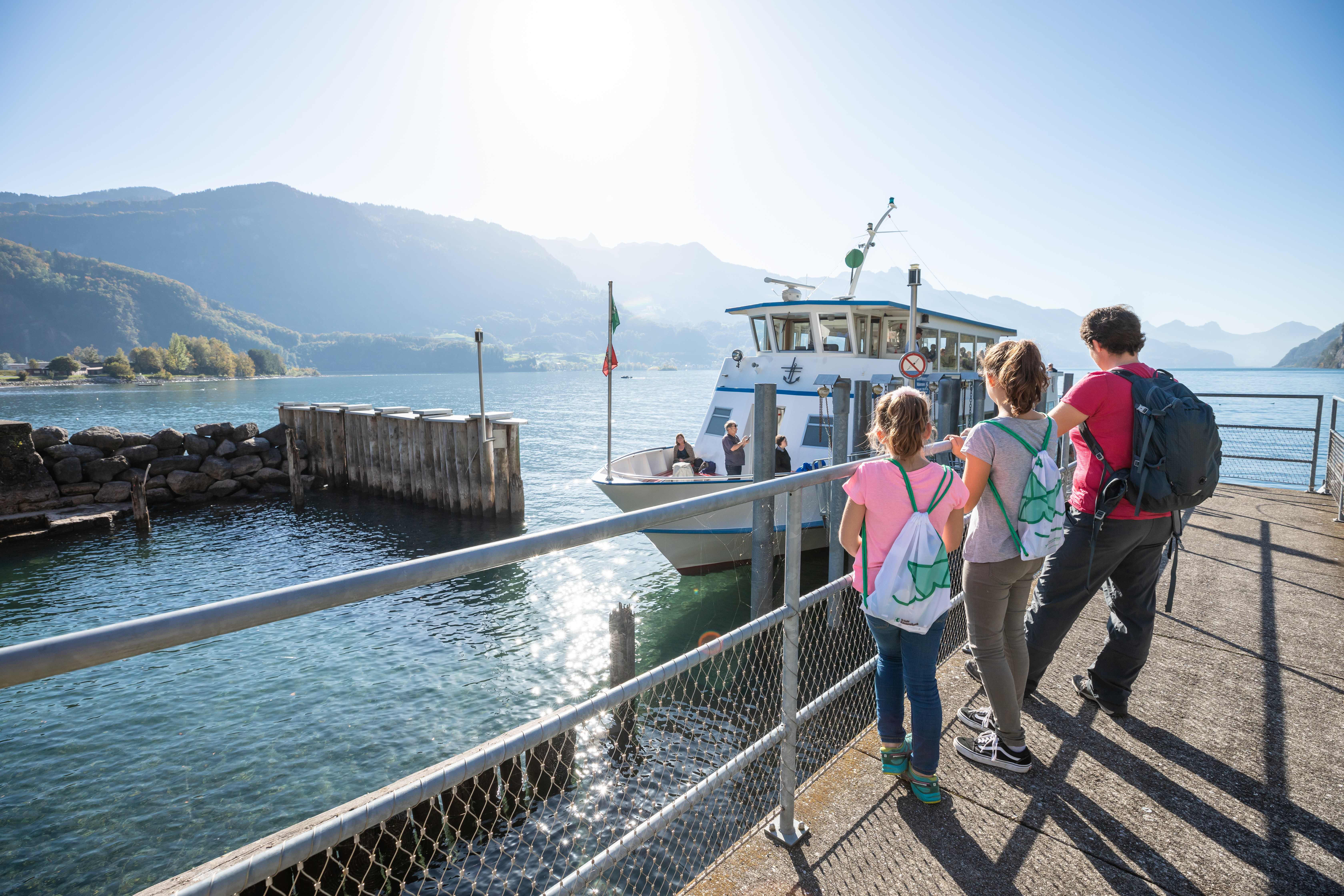 Familie mit Kindern steht am Steg vor einem See während ein Schiff einfährt