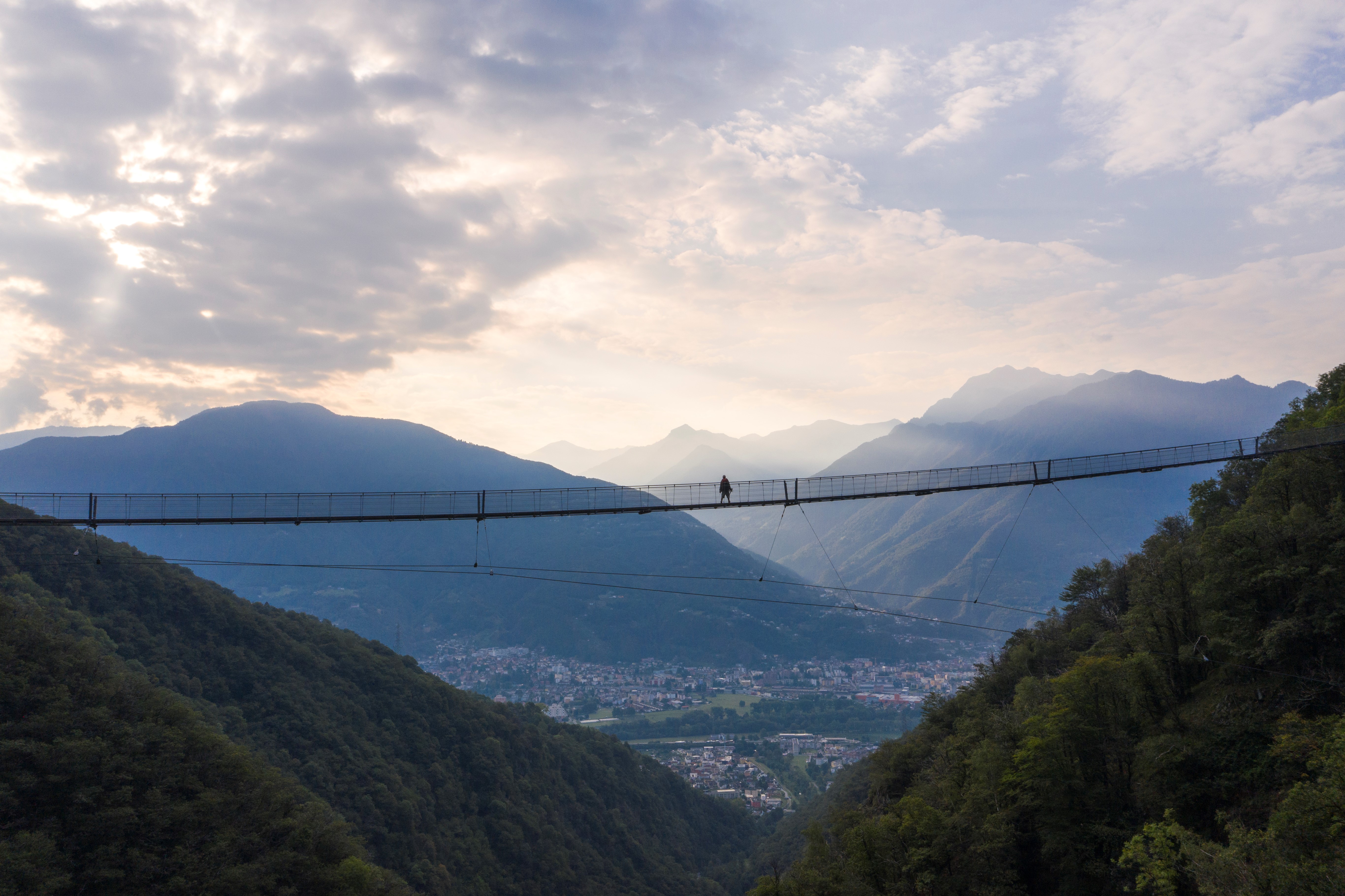 Personne traversant le pont suspendu Ponte Tibetano Carasc, avec vue panoramique sur la vallée et les montagnes du Tessin.