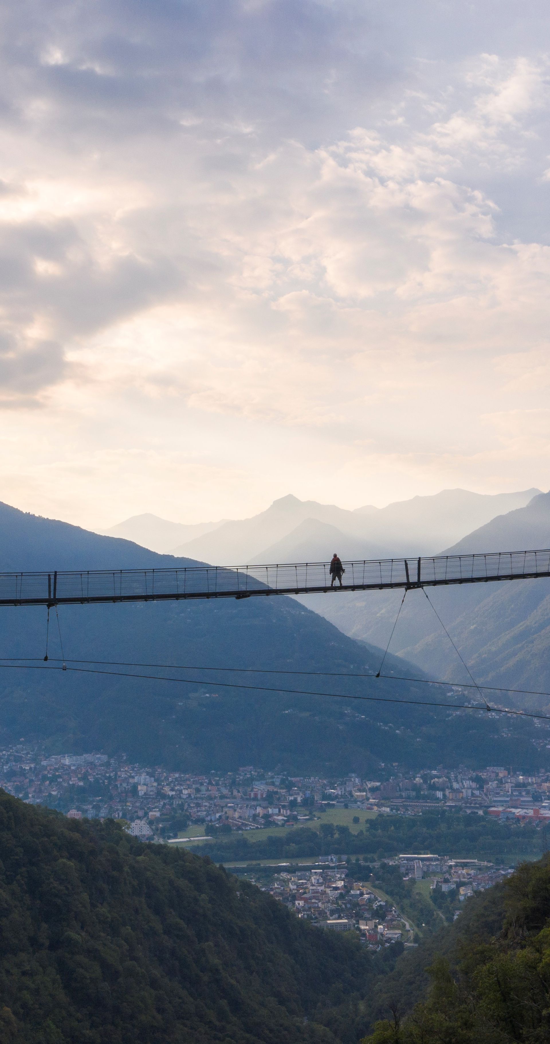 Personne traversant le pont suspendu Ponte Tibetano Carasc, avec vue panoramique sur la vallée et les montagnes du Tessin.