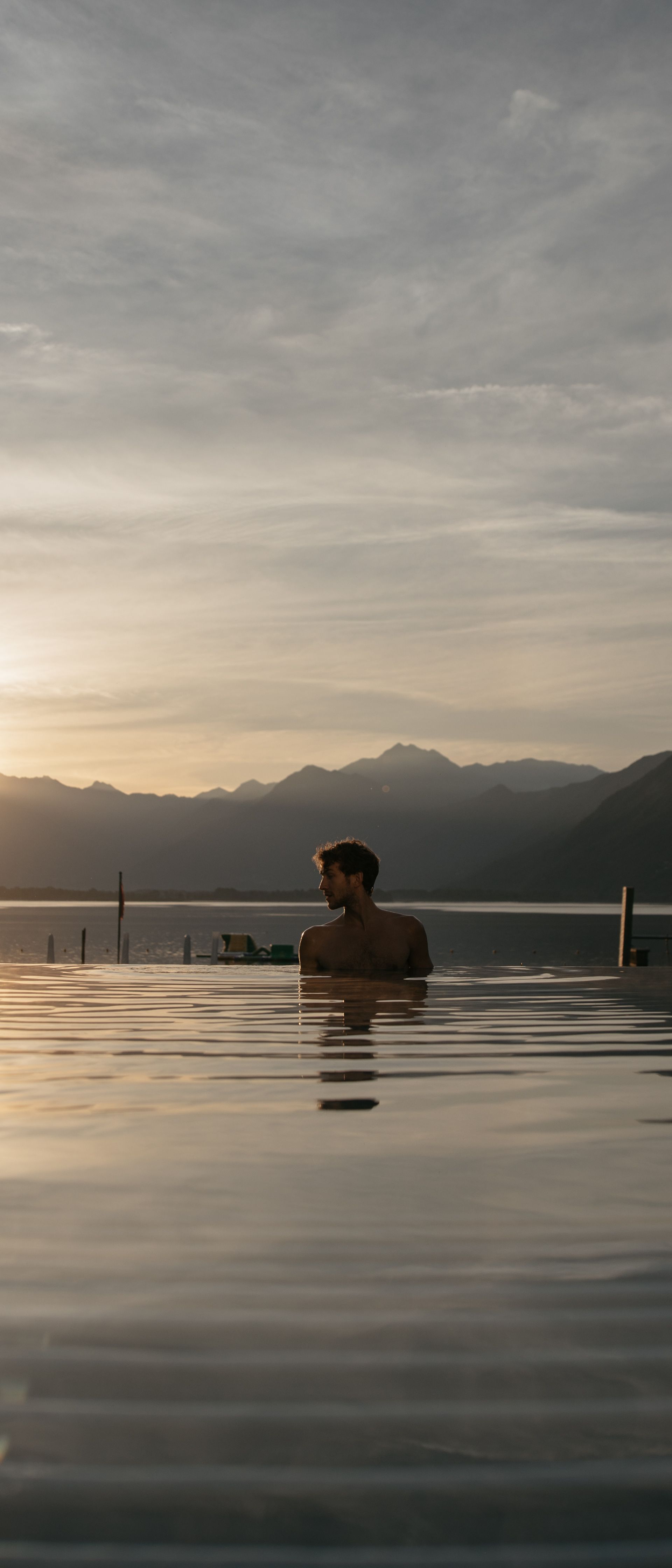 Un uomo si rilassa nella piscina a sfioro delle Termali Salini & Spa Locarno, con vista sul Lago Maggiore al tramonto, circondato da montagne e tranquillità.