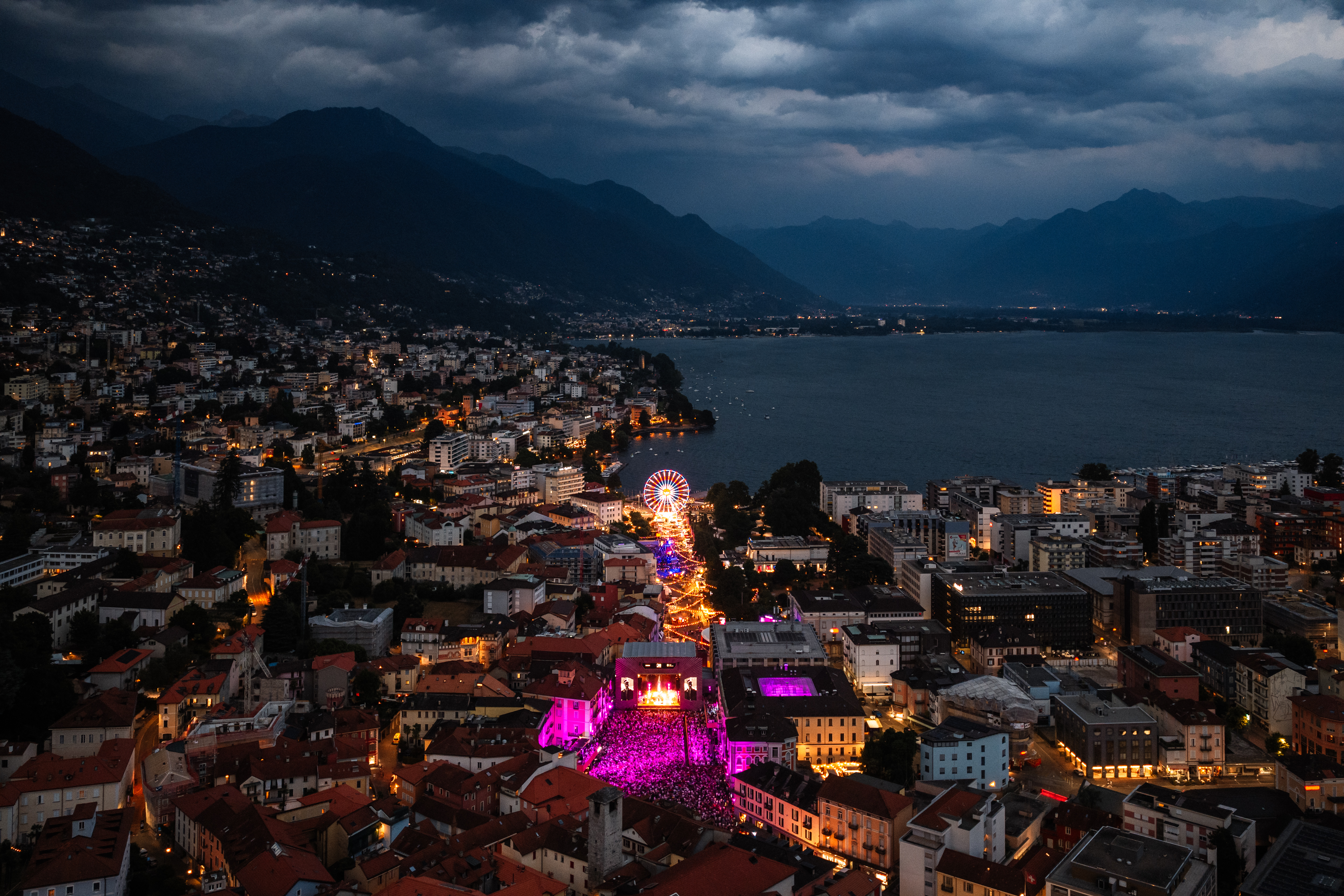 Night aerial view of Locarno with illuminated Moon+Stars festival area, Ferris wheel and Lake Maggiore