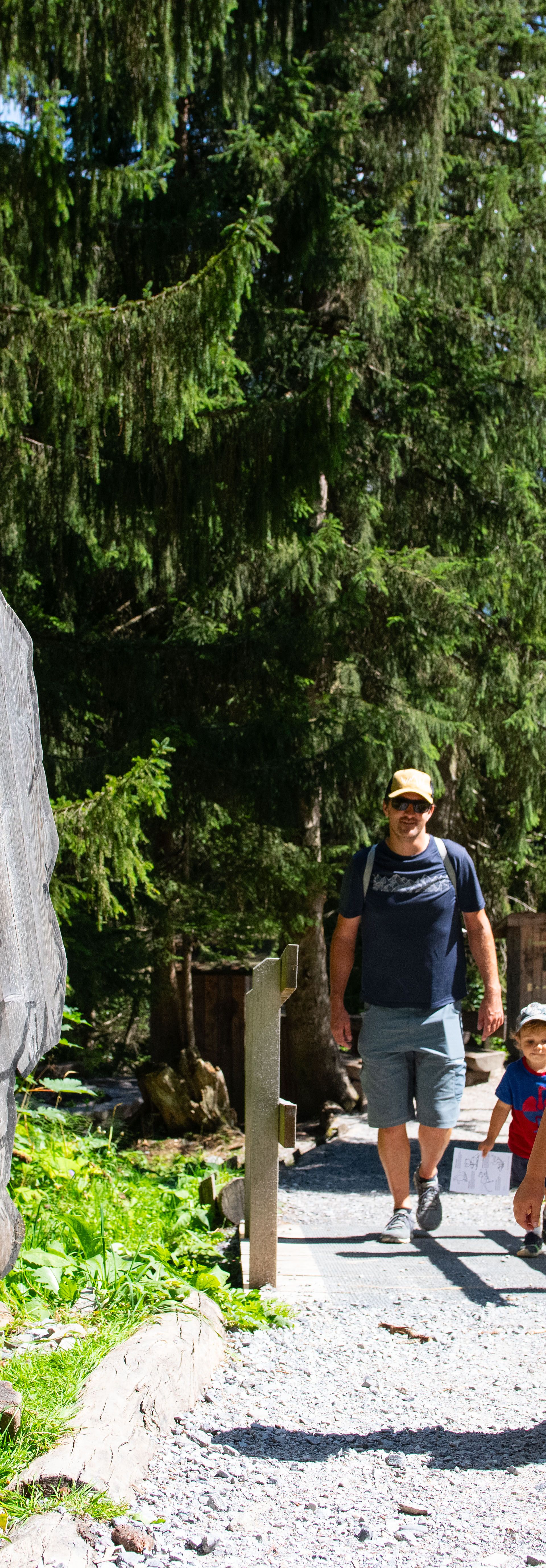 Mehrere Kinder und ein Erwachsener spazieren bei Sonnenschein durch den Riesenwald in Elm – im Vordergrund steht ein hölzernes Riesen-Schild am Waldrand