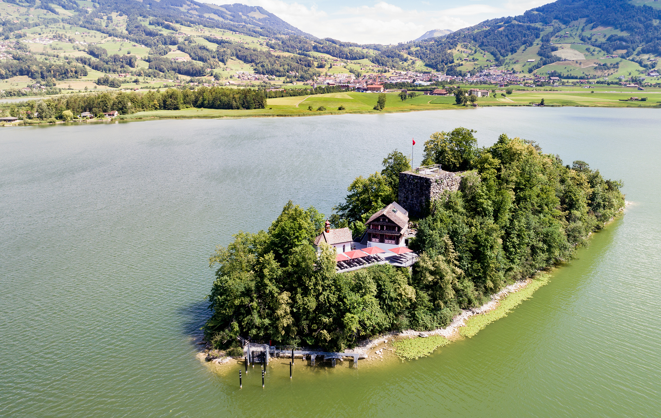 Aerial view of Schwanau Island on Lake Lauerz with its historic inn and castle ruins, surrounded by green water and rolling hills.