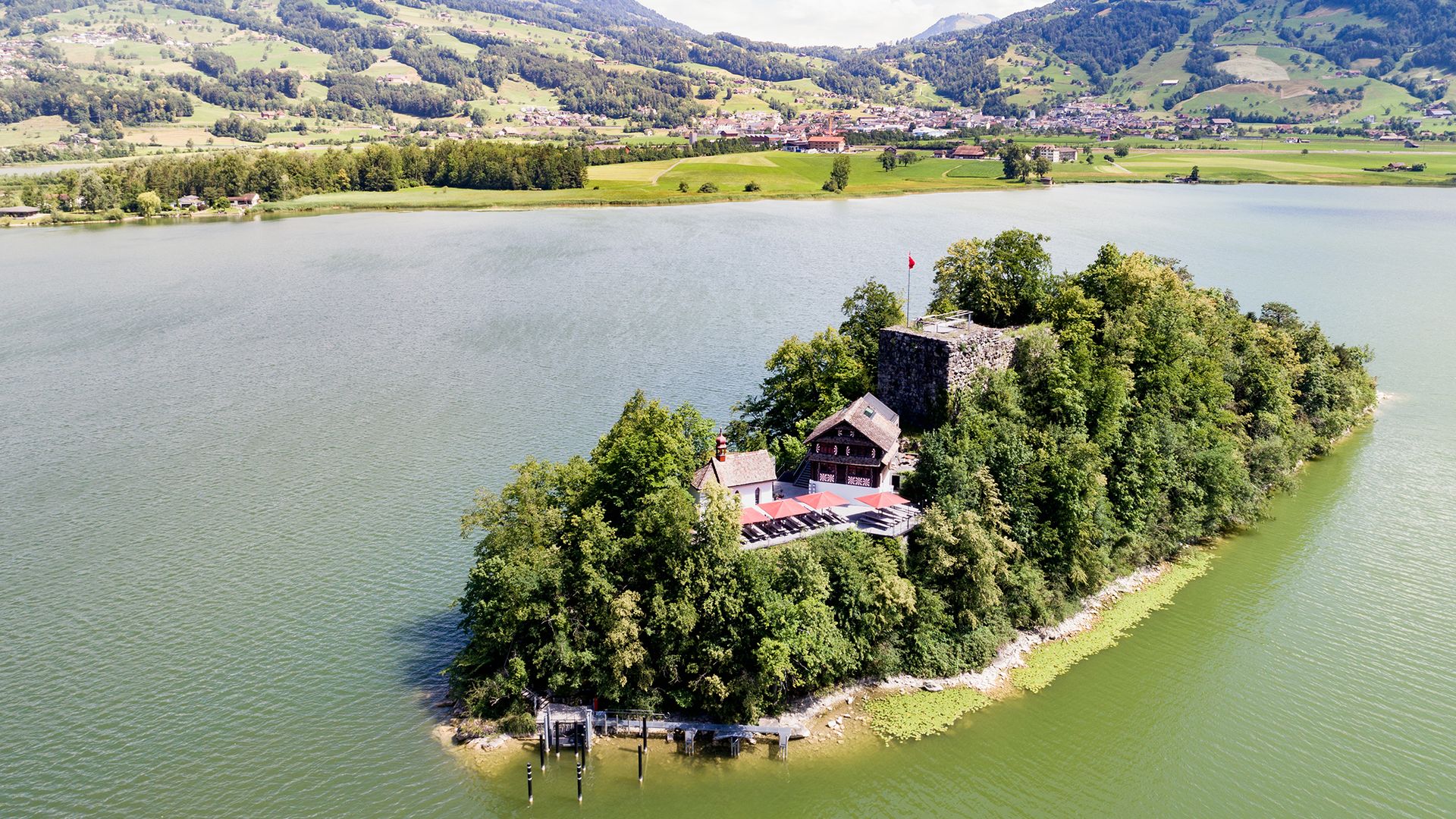 Aerial view of Schwanau Island on Lake Lauerz with its historic inn and castle ruins, surrounded by green water and rolling hills.