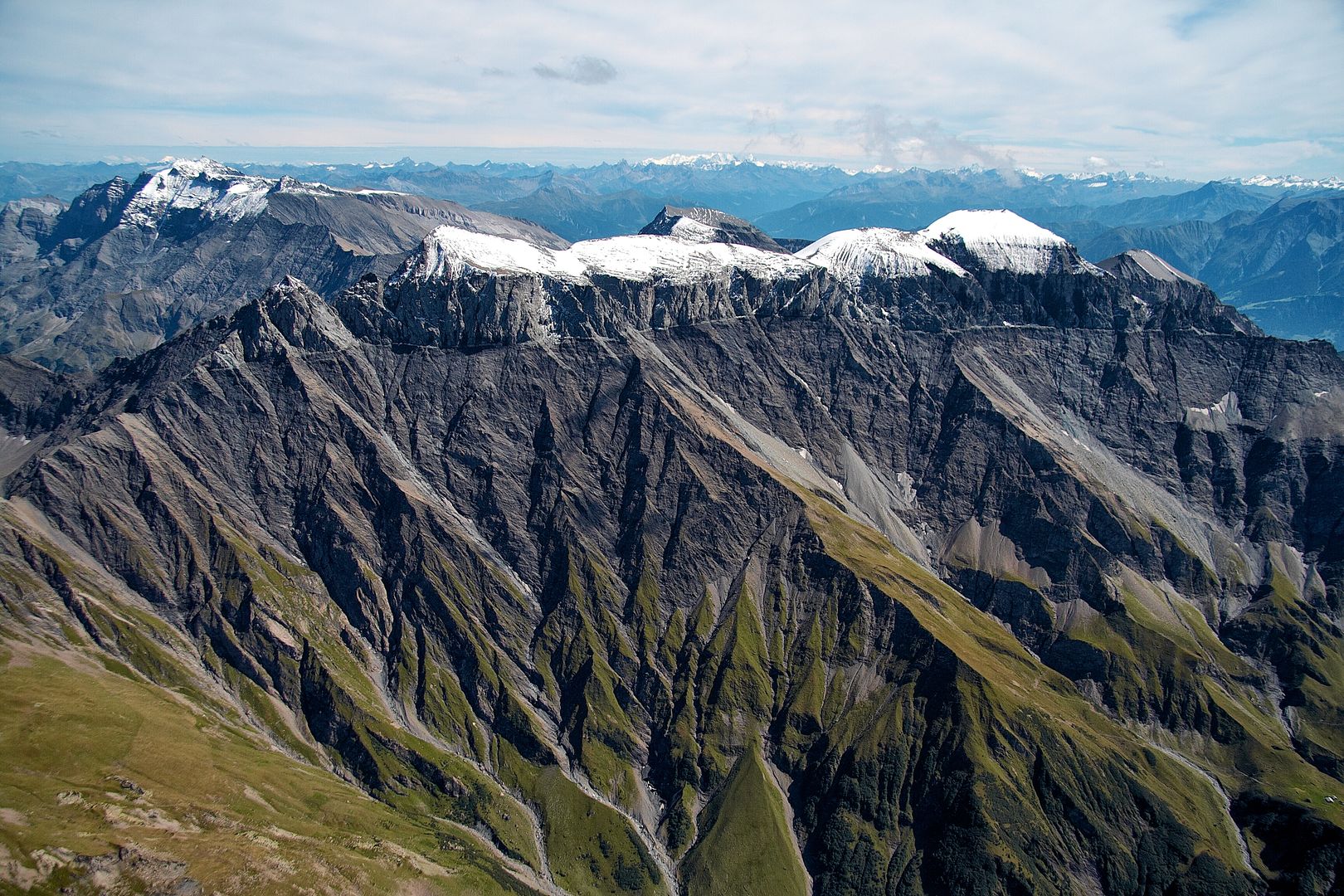 Graues Alpengebirge mit grünen Wiesen und schneebedeckten Gebirgsspitzen