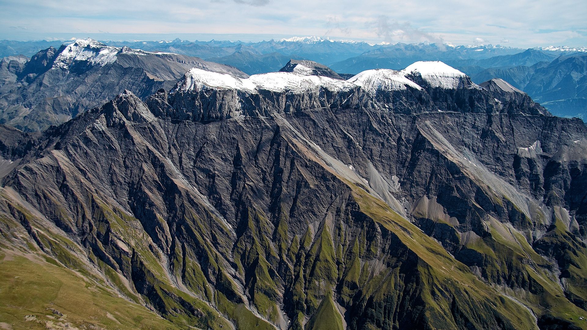 Graues Alpengebirge mit grünen Wiesen und schneebedeckten Gebirgsspitzen