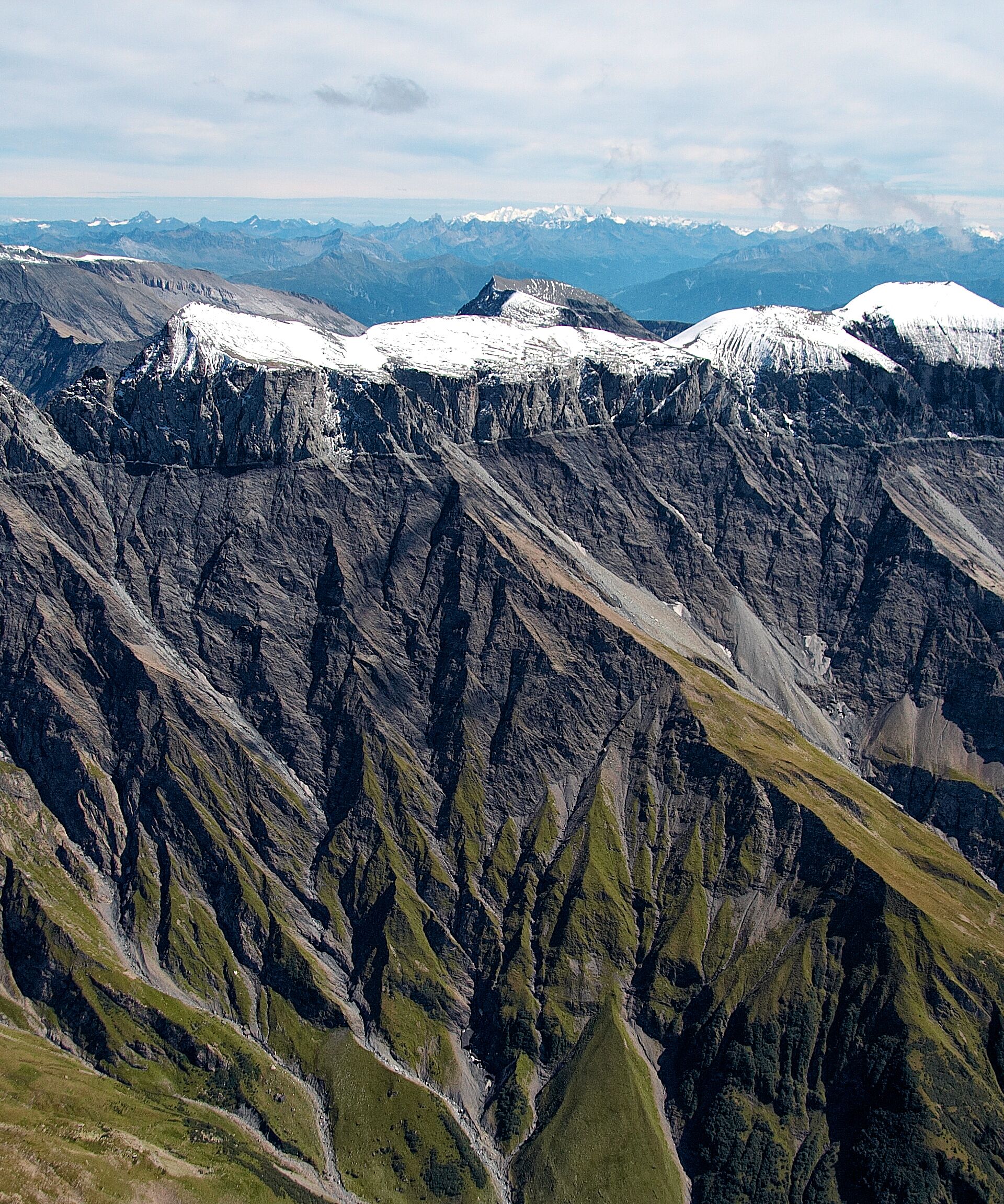 Graues Alpengebirge mit grünen Wiesen und schneebedeckten Gebirgsspitzen