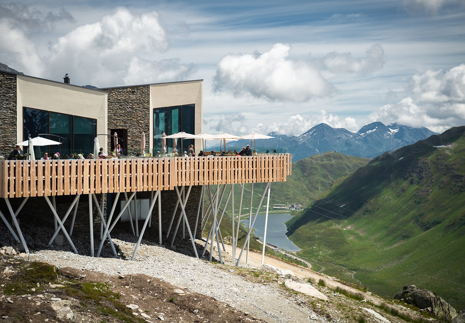 The elegant Restaurant Gütsch with its large sun terrace sits at 2300 m above sea level – guests relax under parasols with panoramic mountain views and Lake Oberalp in the background