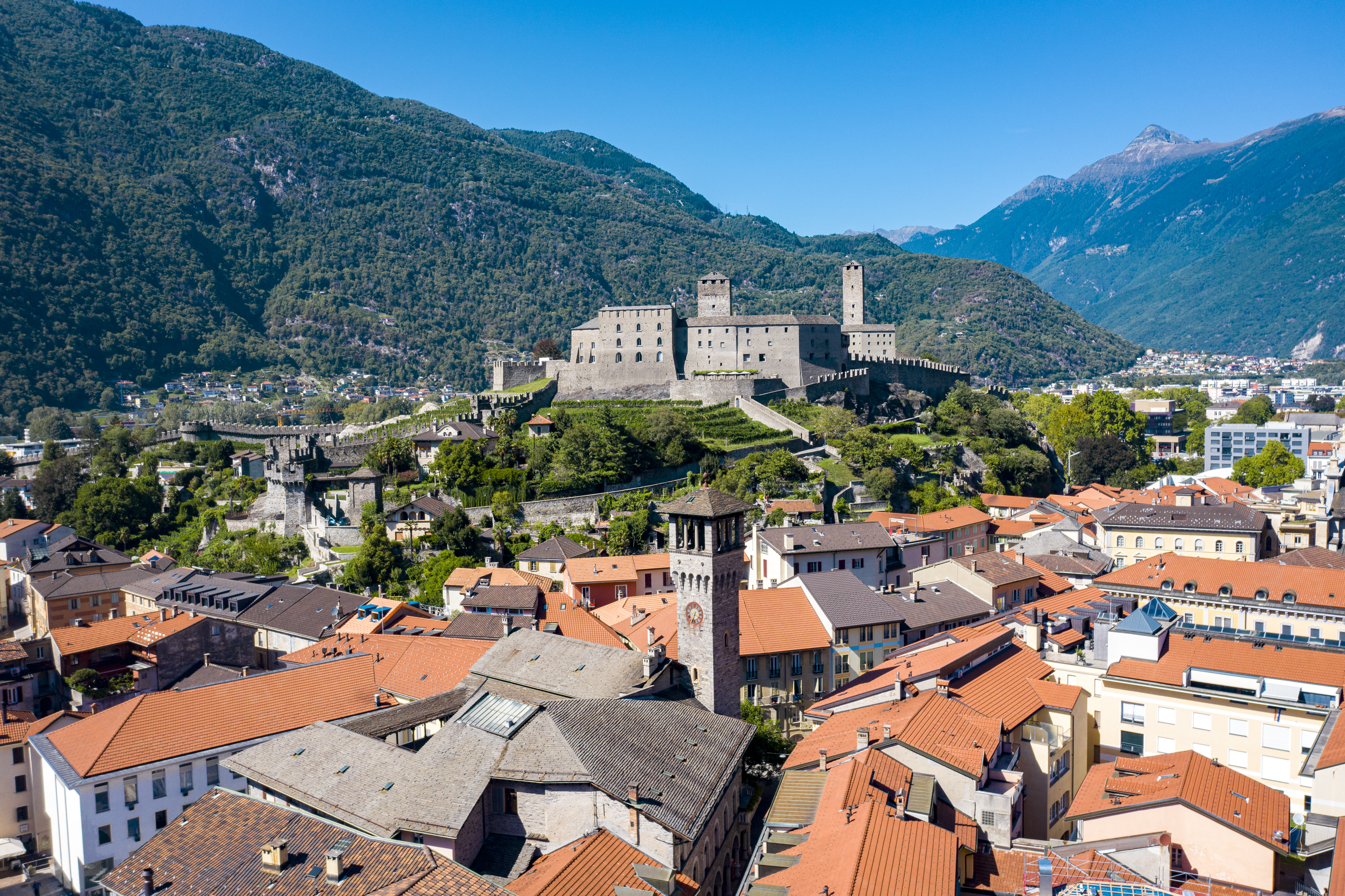 Luftaufnahme von Bellinzona mit der beeindruckenden Burg Castelgrande, umgeben von den historischen Dächern der Altstadt und den grünen Tessiner Bergen.