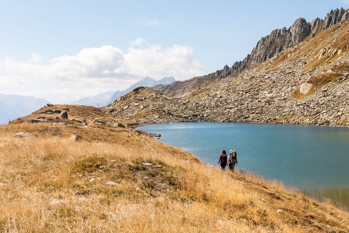 zwei Personen laufen entlang eines Sees in den Bergen