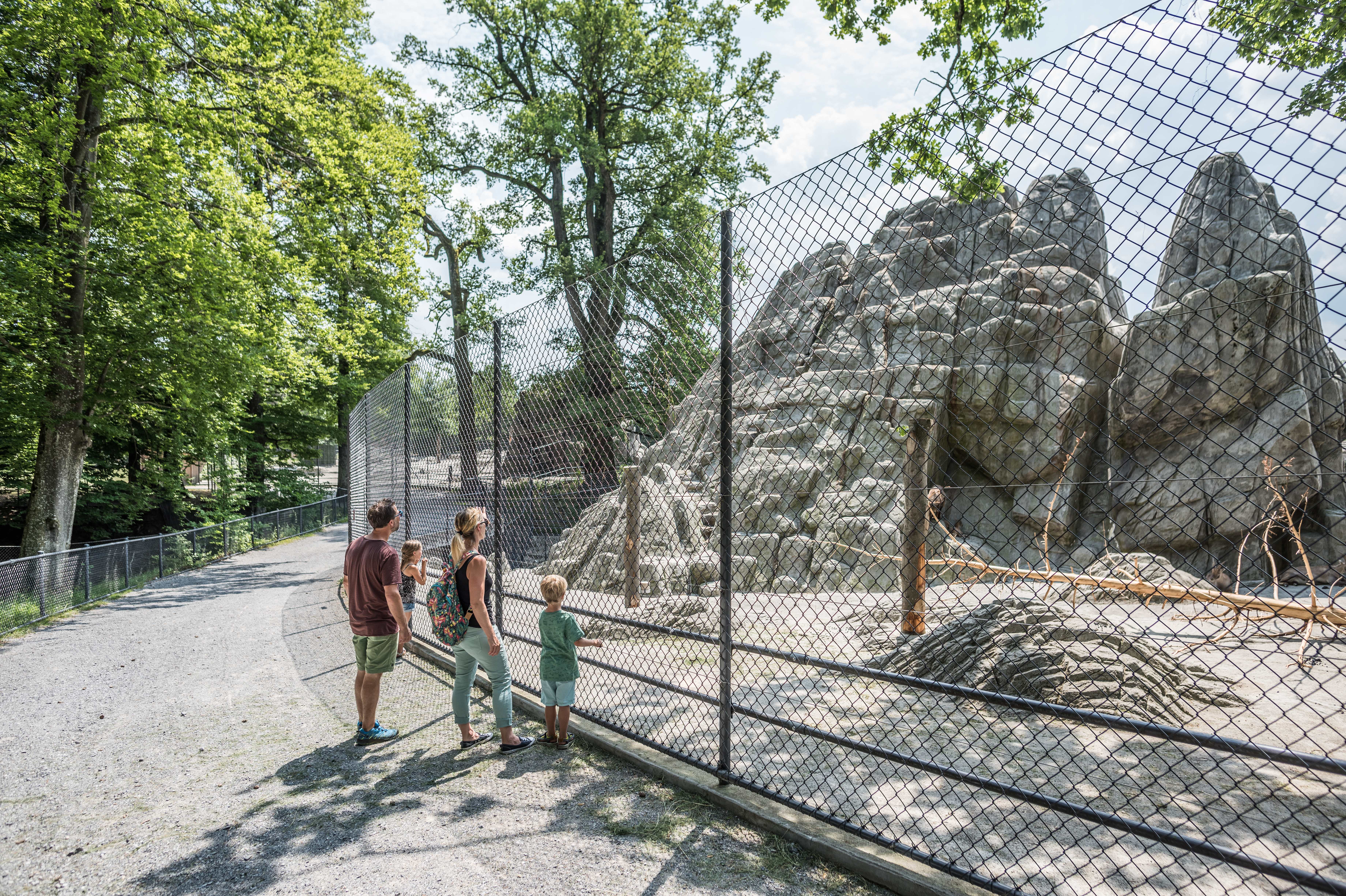 Eine Familie steht vor einem Zaun, hinter ihm ein Tiergehege mit grossen Steinen