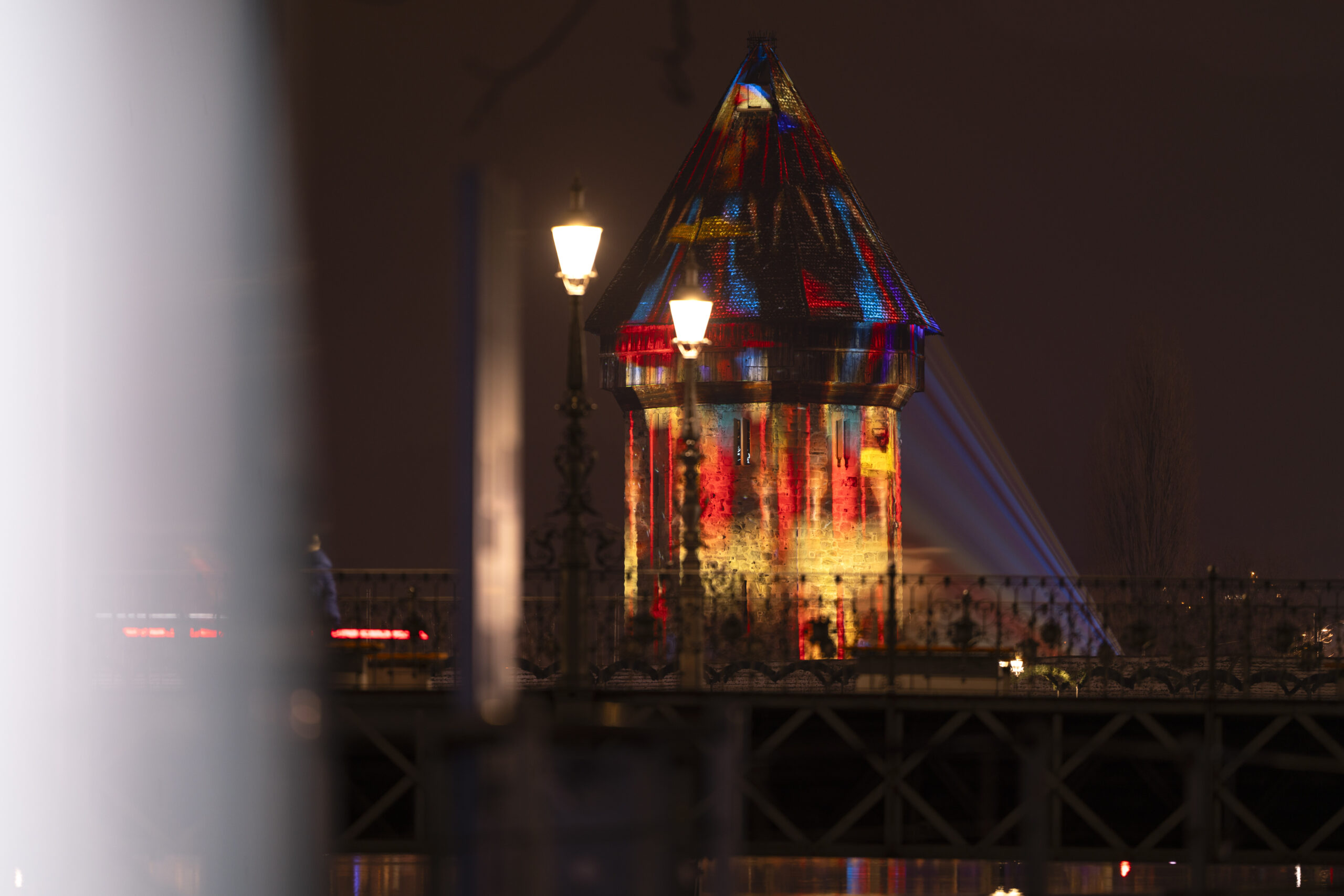 Le château d'eau du pont de la Chapelle à Lucerne, illuminé par des lumières colorées.  