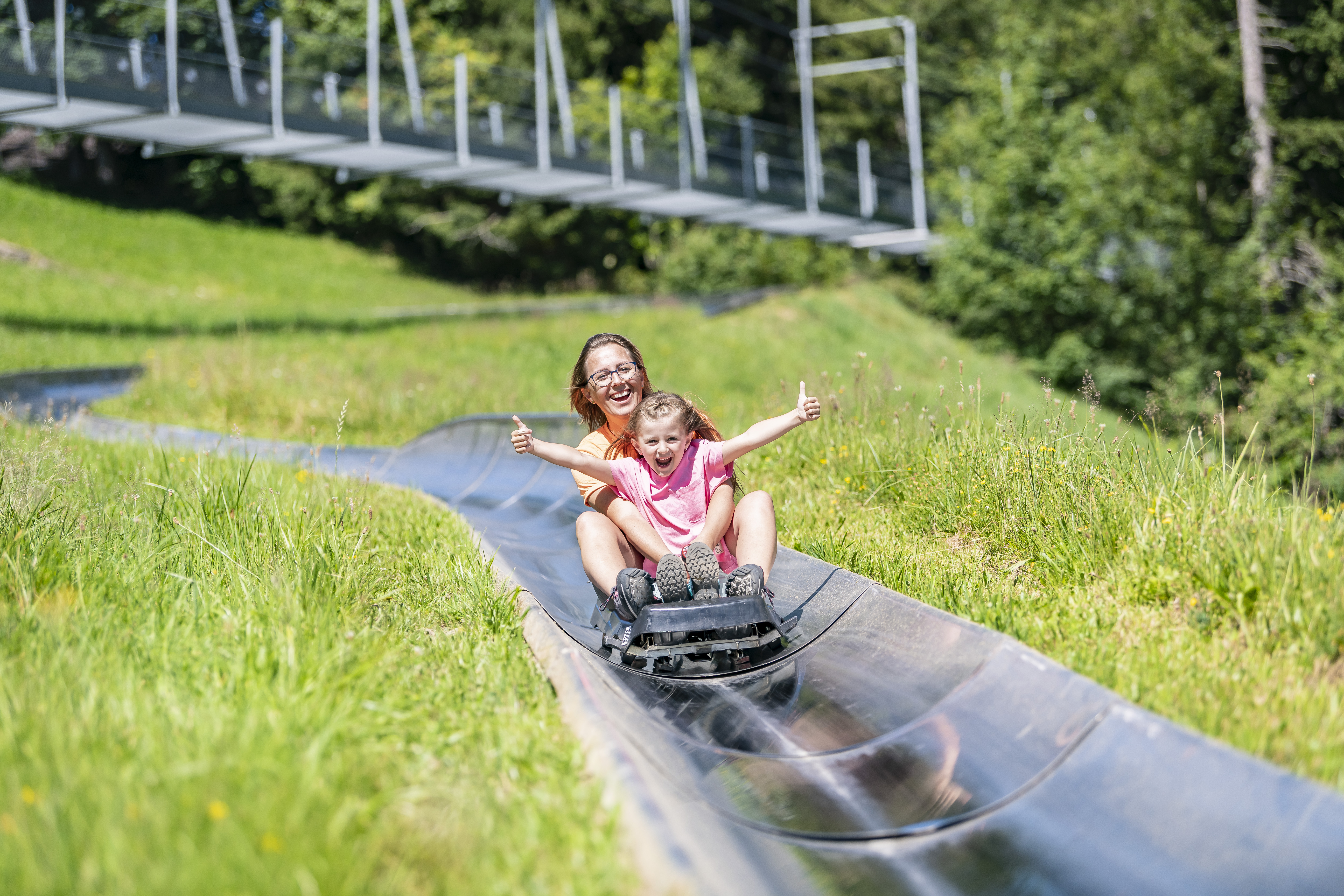 Eine Mutter und ihr Kind auf der Rodelbahn, hinter ihnen eine grüne Wiese