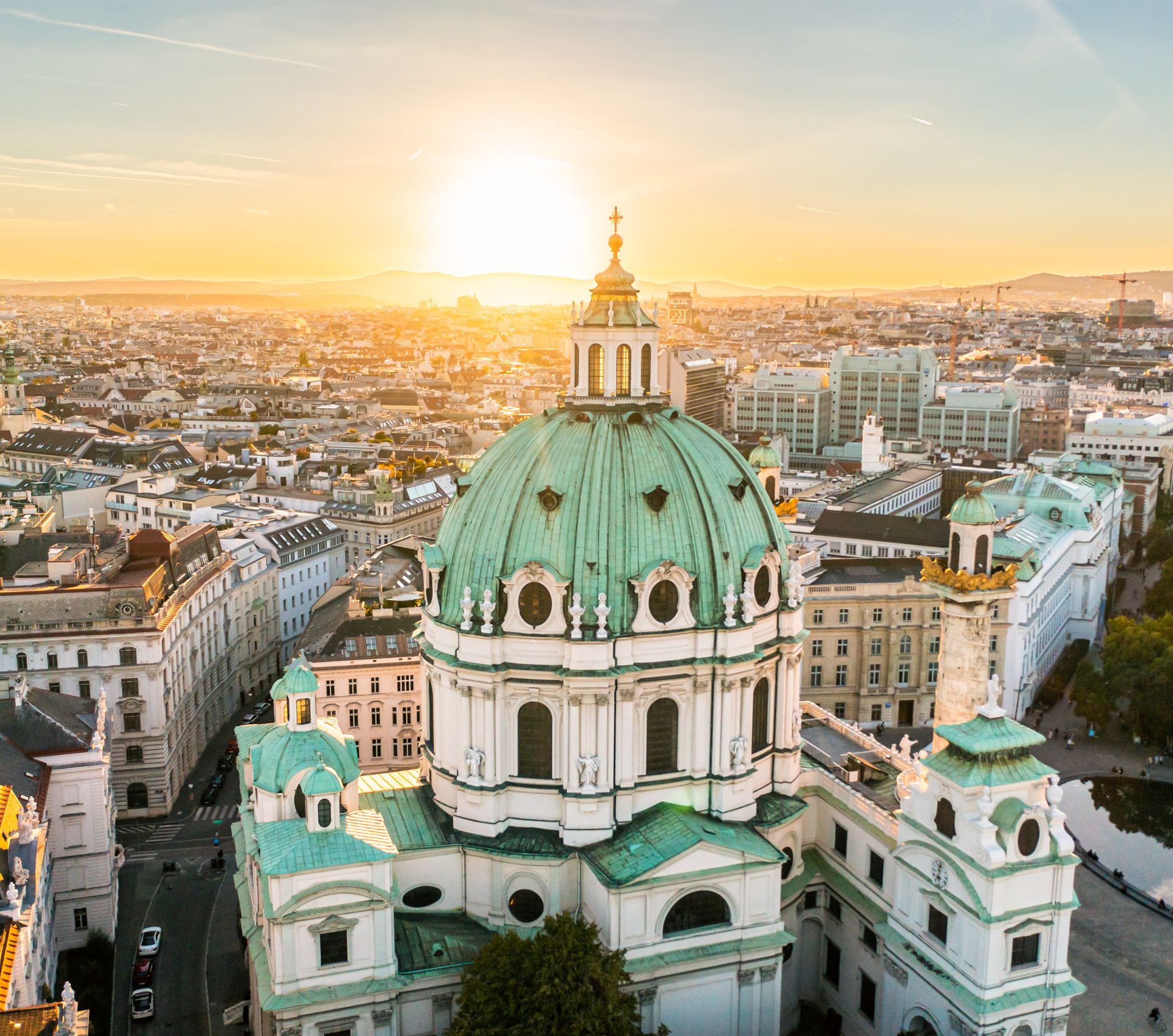 Kirche mit Dom im Vordergrund einer Stadt während die Sonne untergeht