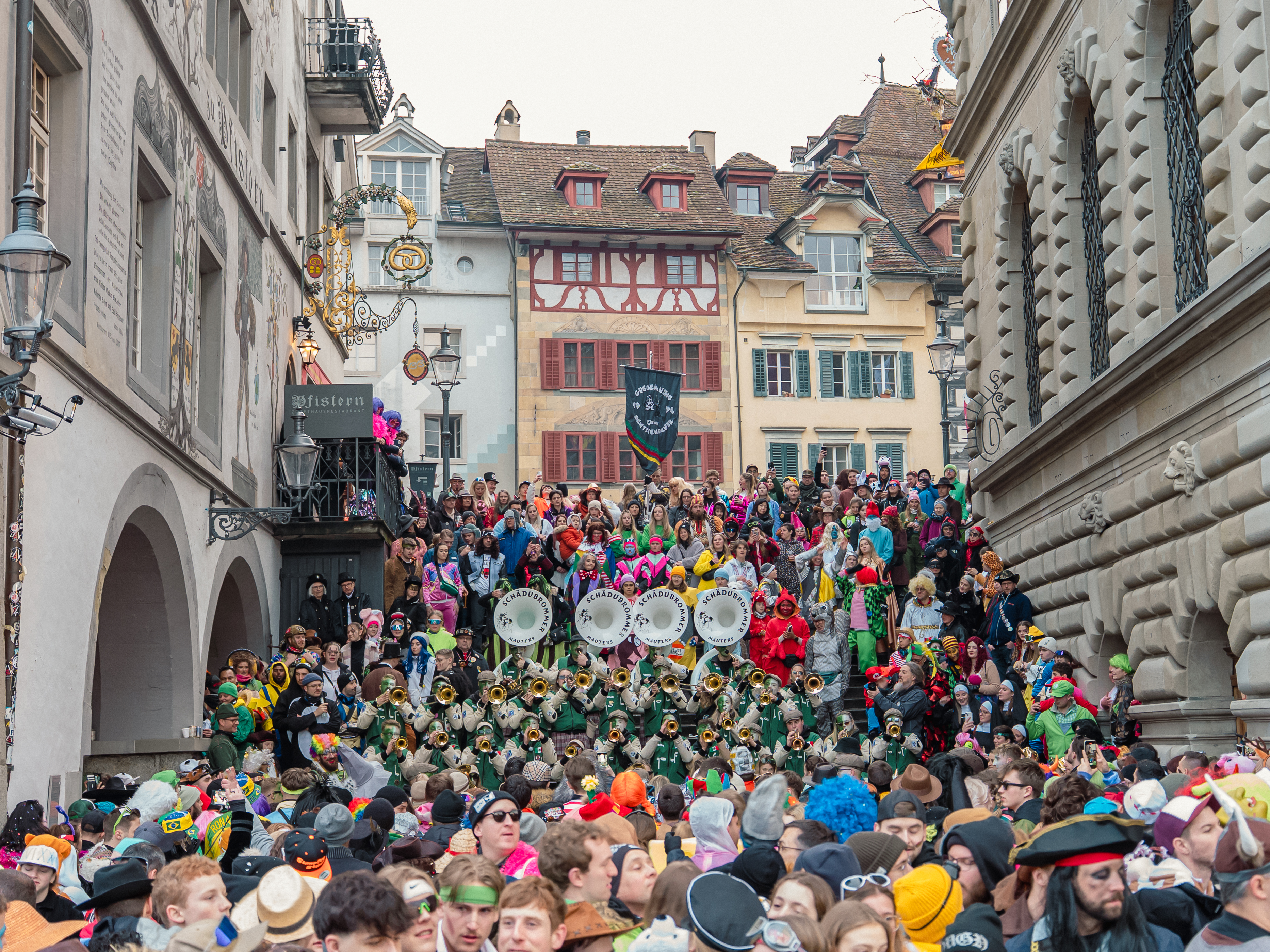 Alt-Text  Rathaustreppe voller Menschen, die während der Fasnacht feiern, während Musik gespielt wird. 