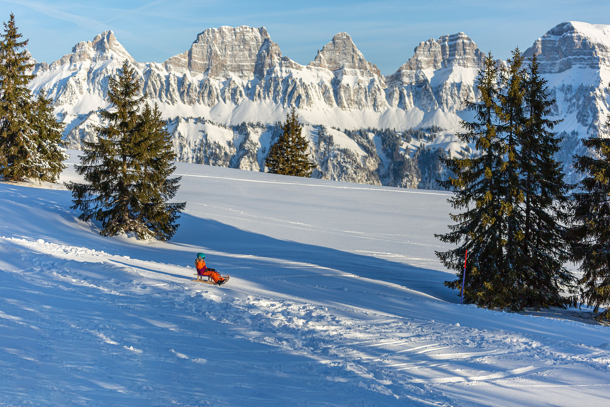 Kind beim Schlitteln am Flumserberg mit Blick auf die verschneiten Churfirsten.