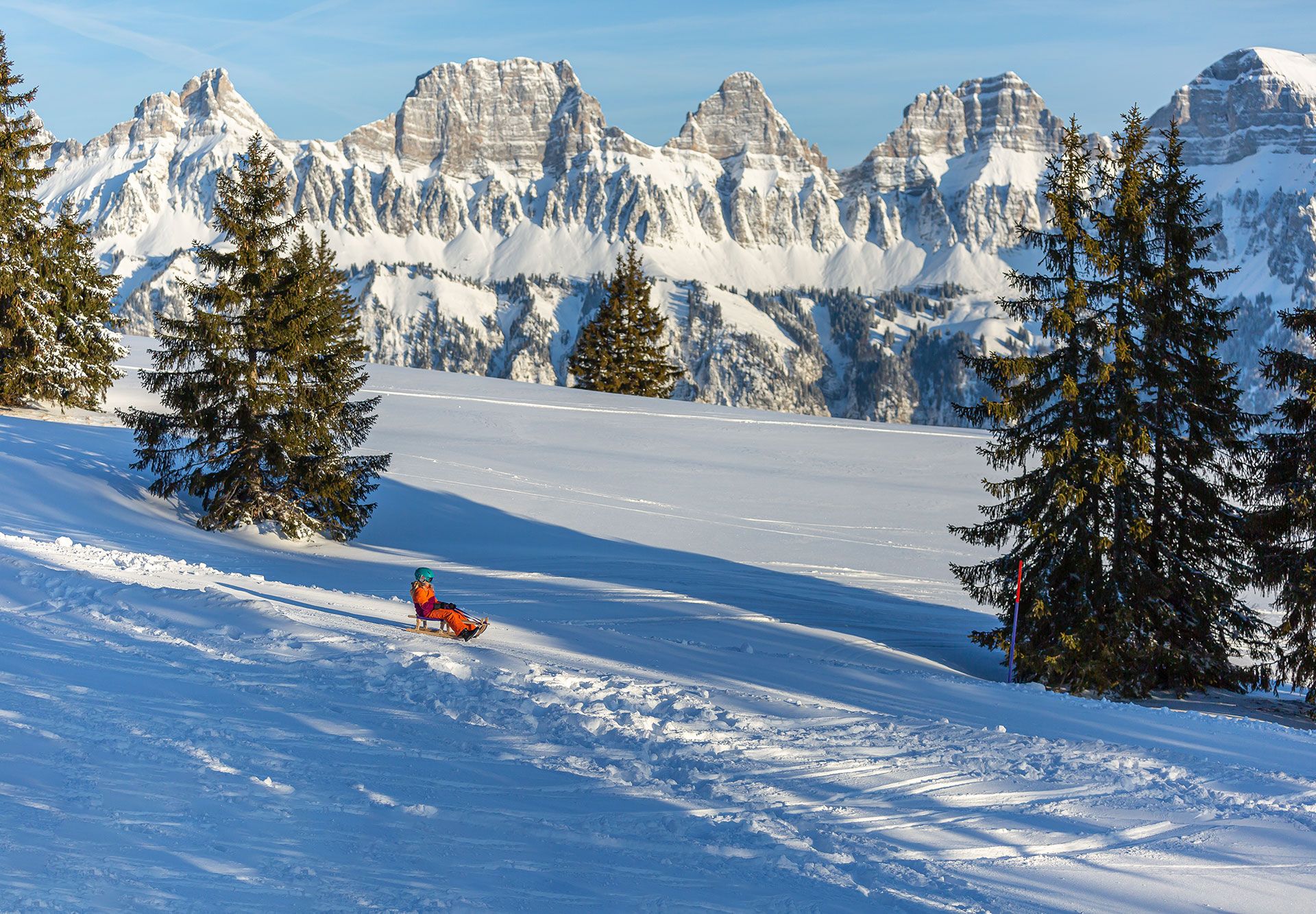 Kind beim Schlitteln am Flumserberg mit Blick auf die verschneiten Churfirsten.