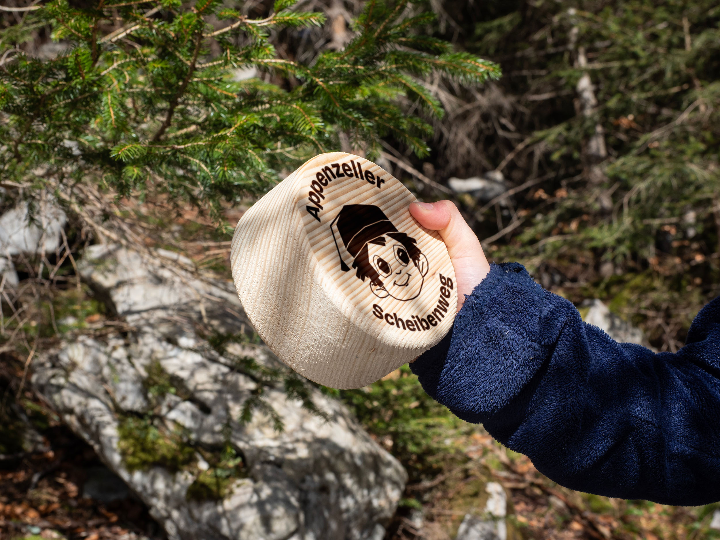 Une main d'enfant tient le « Holzmutschli » du sentier des cibles d'Appenzell.