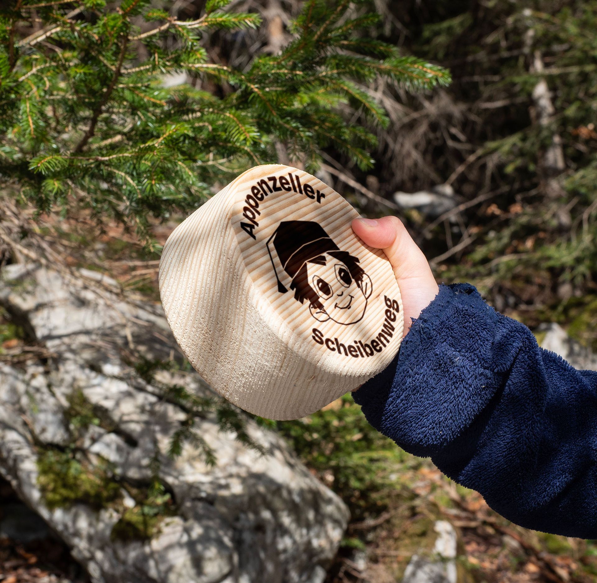 Kinderhand hält das Holzmutschli des Appenzeller Scheibenwegs.