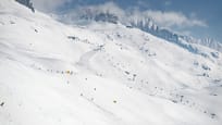 Diverse Skipisten, ein Sessellift und eine Gondelbahn, im Hintergrund eine verschneite Bergkette