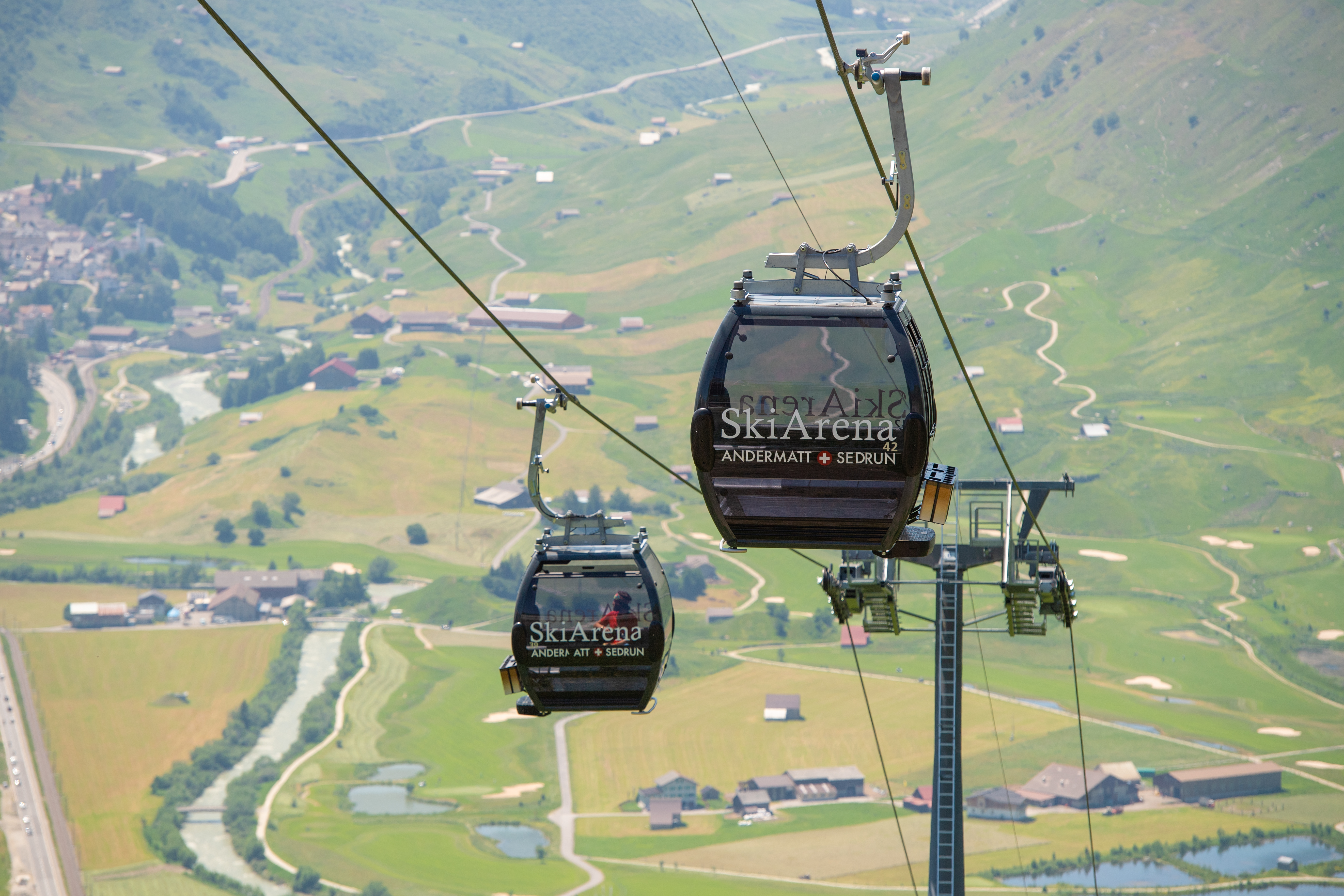 Zwei schwarze Gondeln des Gütsch-Express’ mit dem Andermatt Swiss Alps Golf Course und der Reuss im Hintergrund