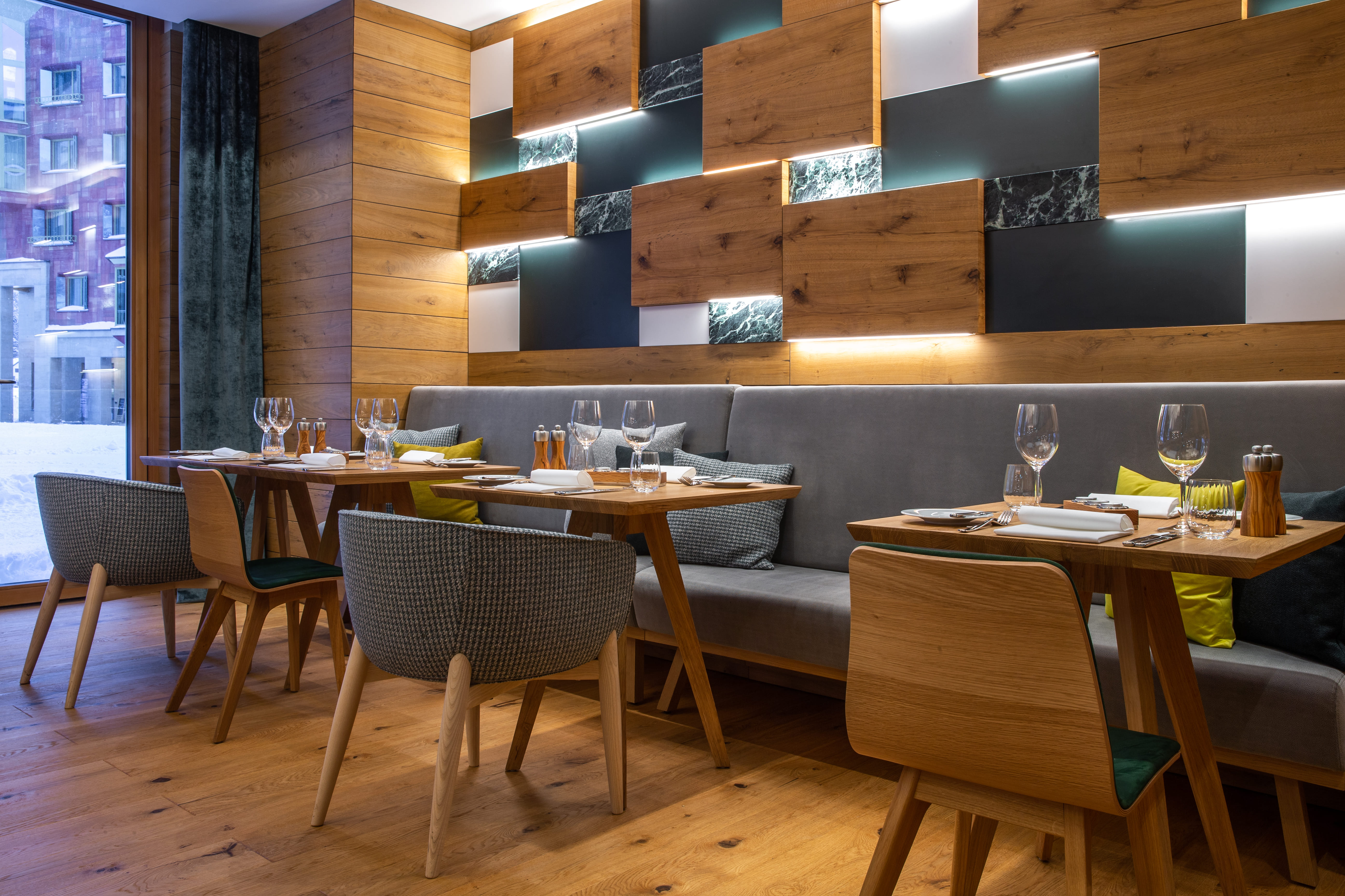 Restaurant area with wooden tables, upholstered chairs, and a wall featuring illuminated wood and stone panels at Radisson Blu Hotel Reussen in Andermatt