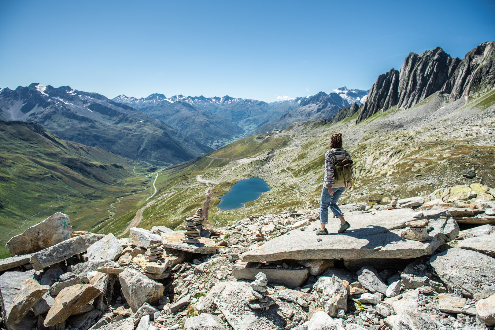 Eine Person sieht sich in Andermatt beim Wandern einen Bergsee an.
