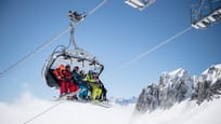 Chairlift with six winter sports enthusiasts above the clouds, heading toward Schneehüenerstock