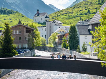mys-Dorfführungen Urserntal-Dorfführung auf Brücke mit Kapelle im Hintergrund Dorfführungen Urserntal