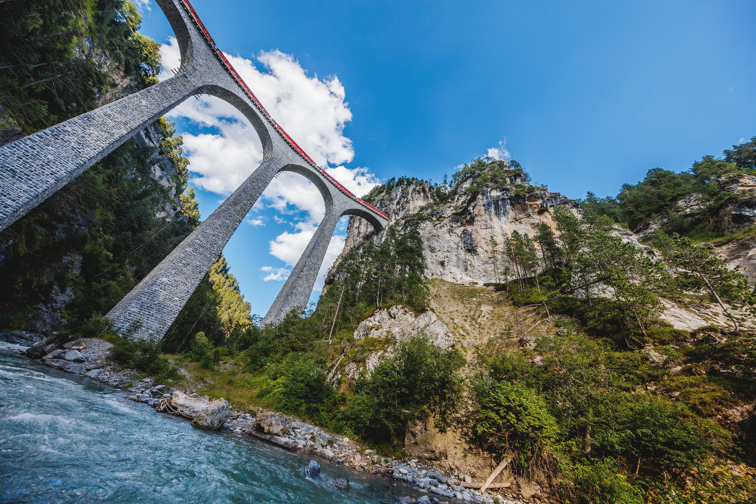 A red RhB train crosses the Landwasser Viaduct and the river flows below.