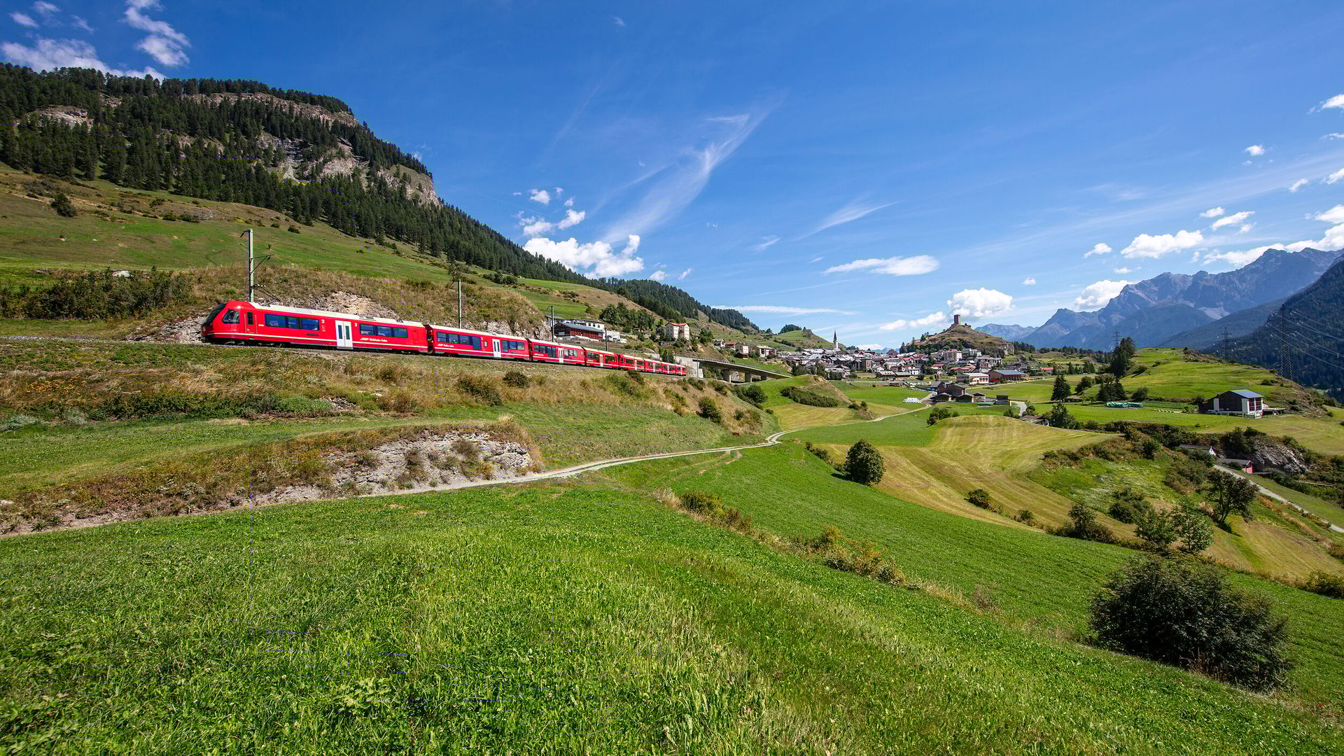 A regional train passes through the Engadin and the village of Ardez can be seen in the background.