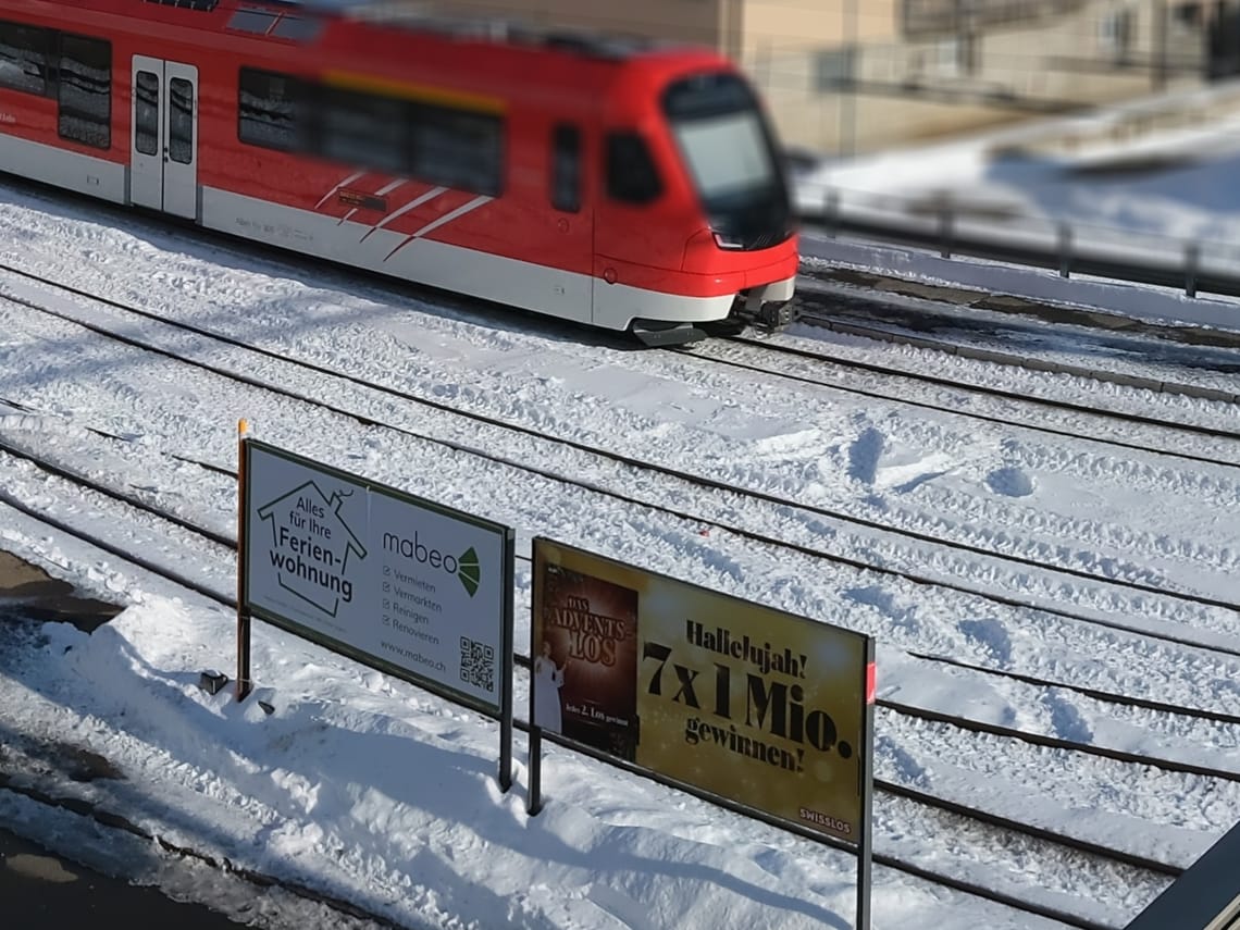 Realp, Winter Der Realp-Zug fährt an einem sonnigen Tag durch eine verschneite Stadt.