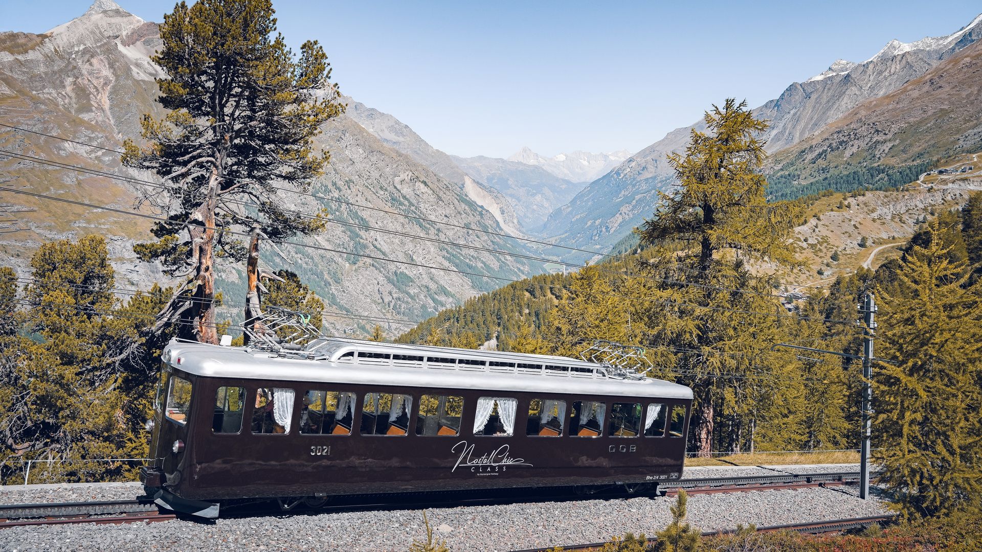 The NostalChic Class wagon, surrounded by forest, rolls under a bright blue sky on a summer's day.