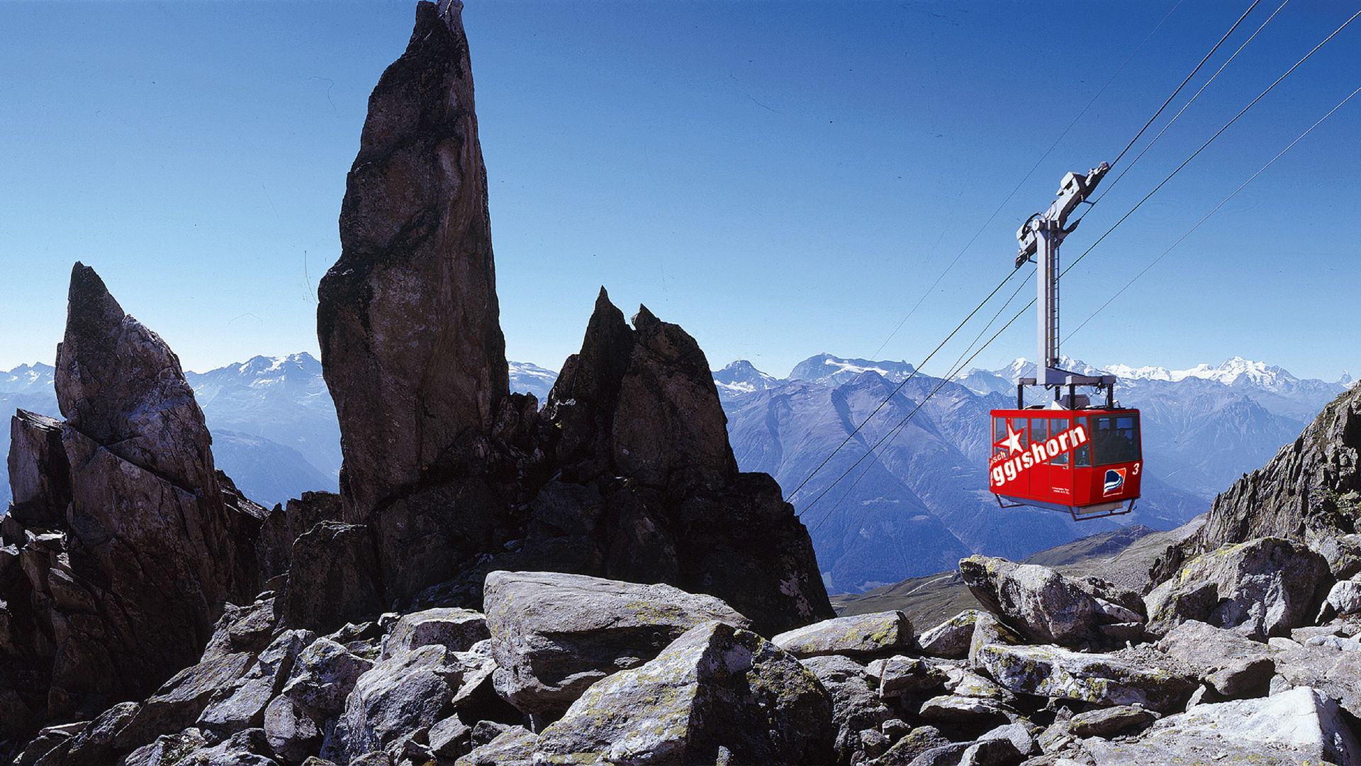 Die rote Eggishorn-Seilbahn erhebt sich in einer Berglandschaft unter einem klaren blauen und wolkenlosen Himmel.
