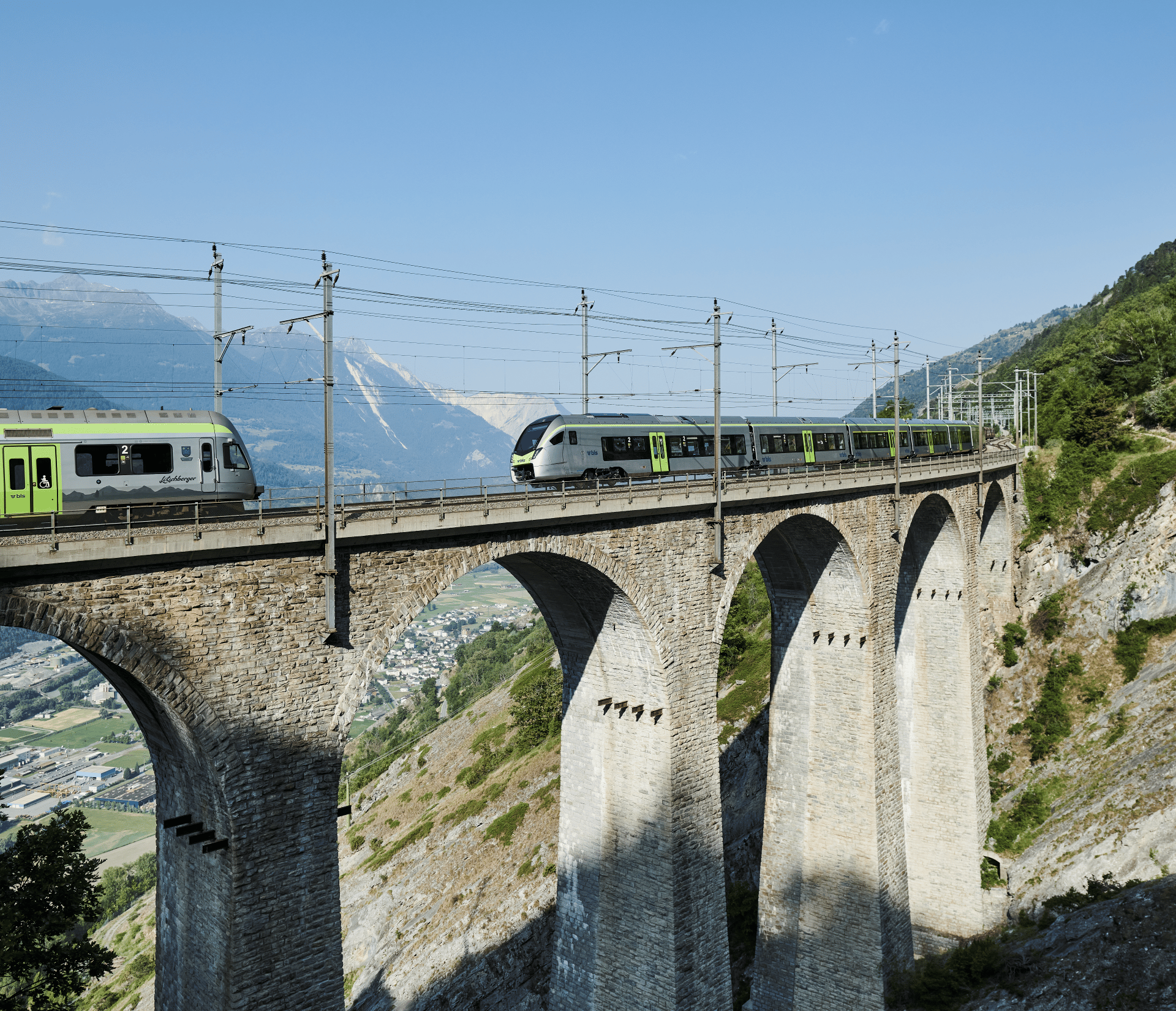 BLS trains cross a bridge on a sunny summer's day, under a cloudless blue sky.