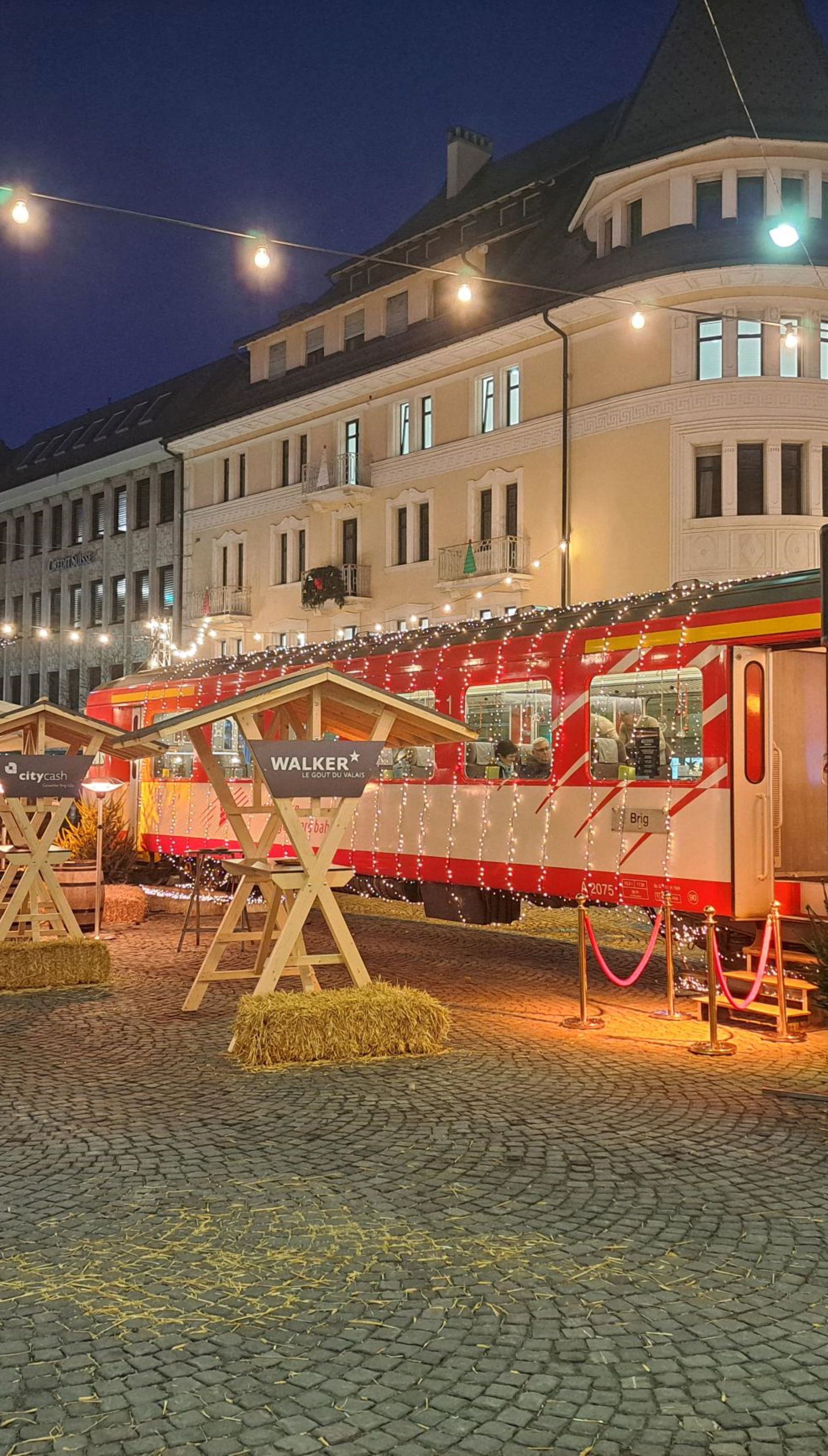 Le train de Noël du Matterhorn Gotthard Bahn, rouge et décoré de lanternes, à Brigue pendant le marché de Noël.
