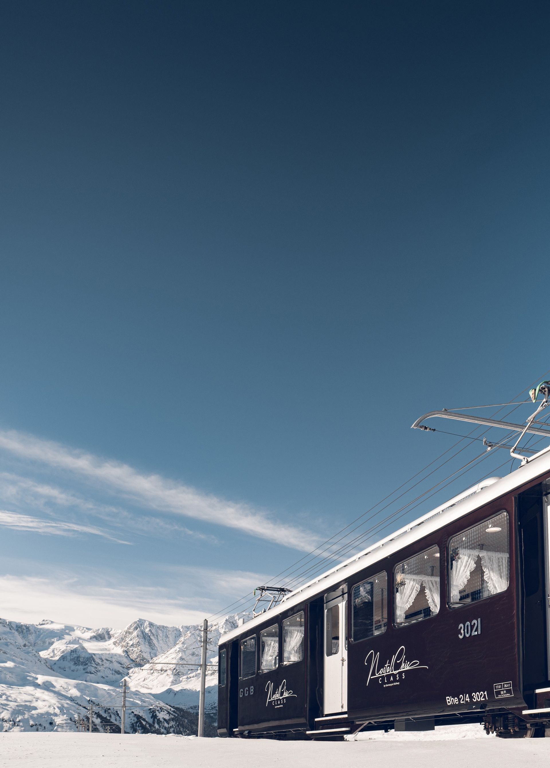 Wagon brun du Nostalchic Class en hiver, sous un ciel bleu, traversant un paysage enneigé avec le Cervin en arrière-plan.