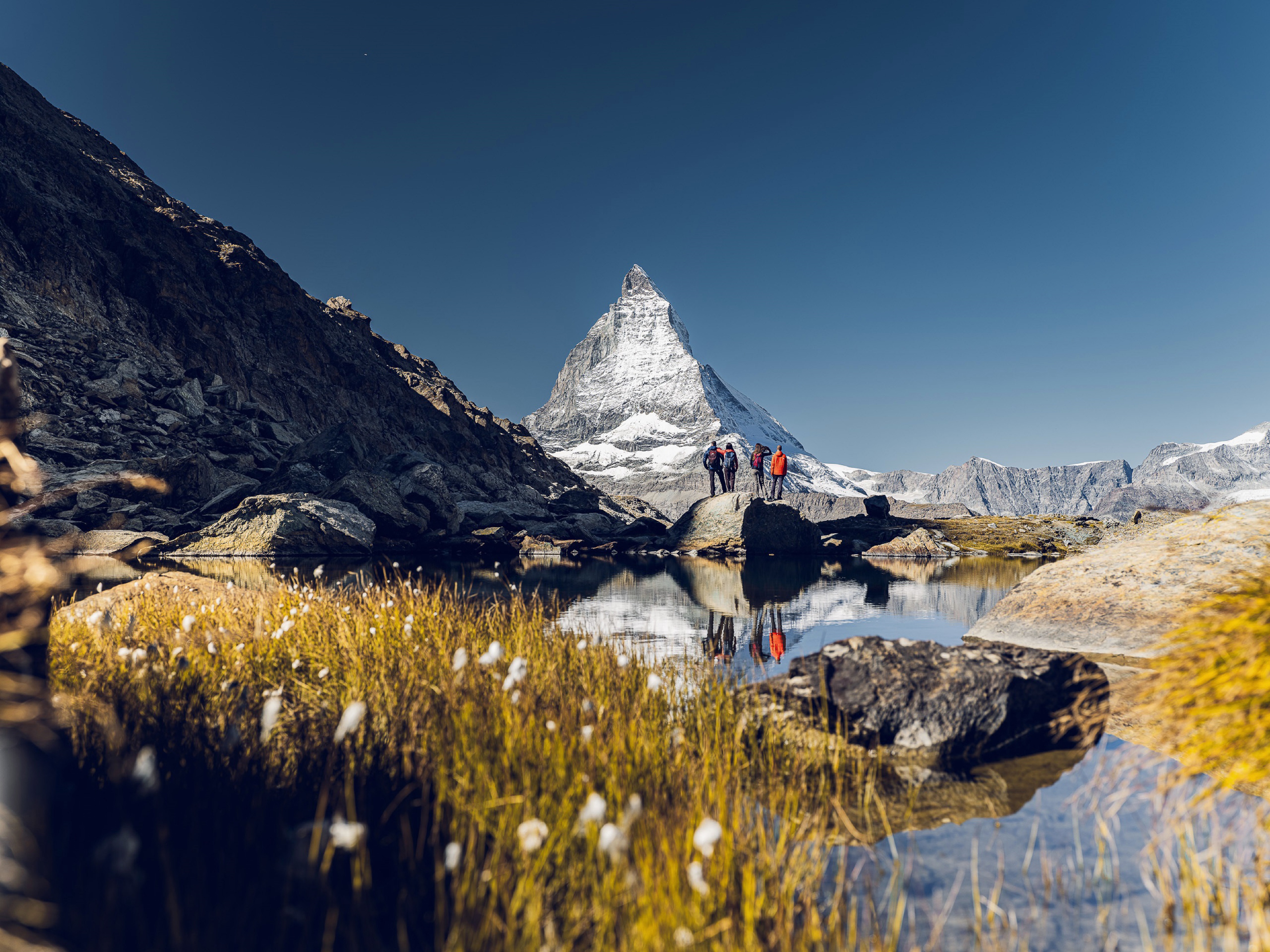 Hikers in front of the Matterhorn, behind the Riffelsee, on a sunny summer's day.