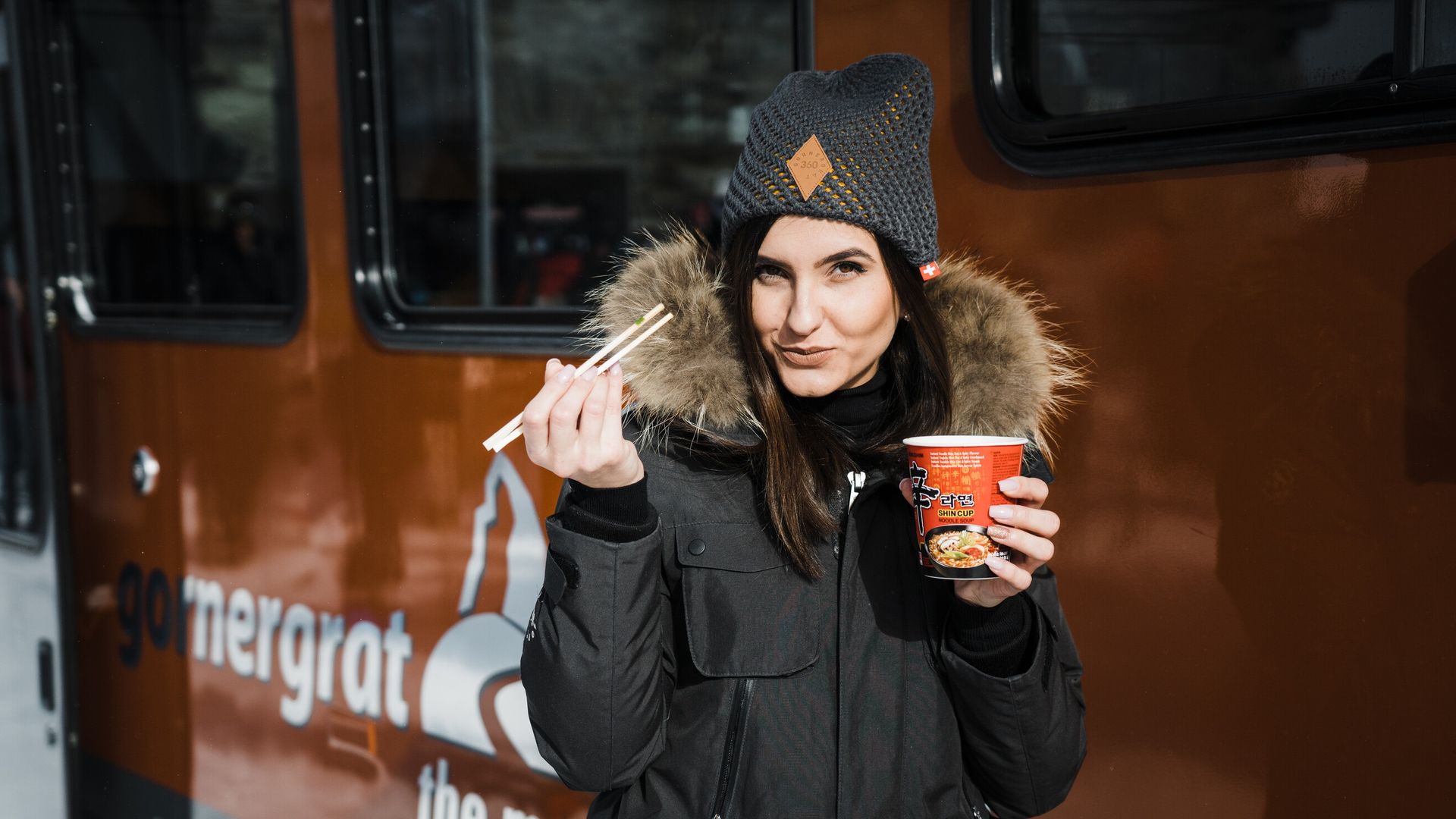 Une femme déguste une soupe de nouilles devant le Gornergrat Bahn en plein hiver.