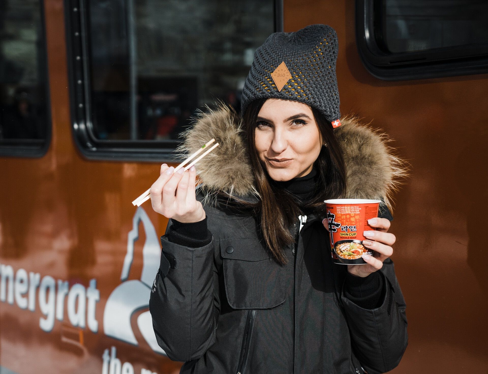 A woman enjoys a noodle soup in front of the Gornergrat Bahn in the middle of winter.