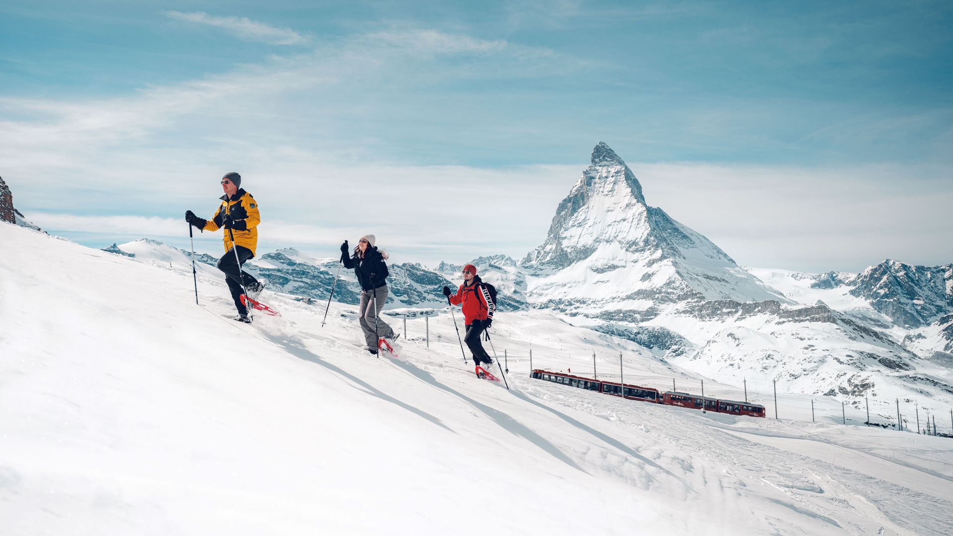 Trois personnes marchent en raquettes dans un paysage enneigé, avec en arrière-plan le Gornergrat Bahn et le Cervin.