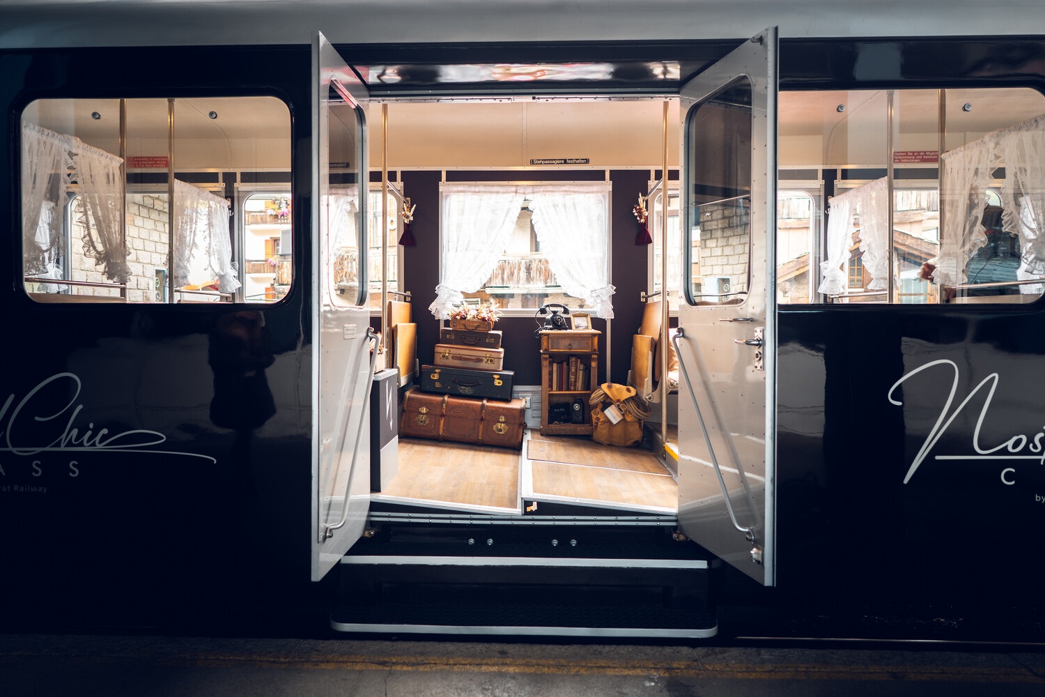 Entrance to NostalChic Class, Gornergrat Bahn The NostalChic Class carriage is in the station, doors open, revealing a retro decor with old suitcases and telephone, creating a warm atmosphere.