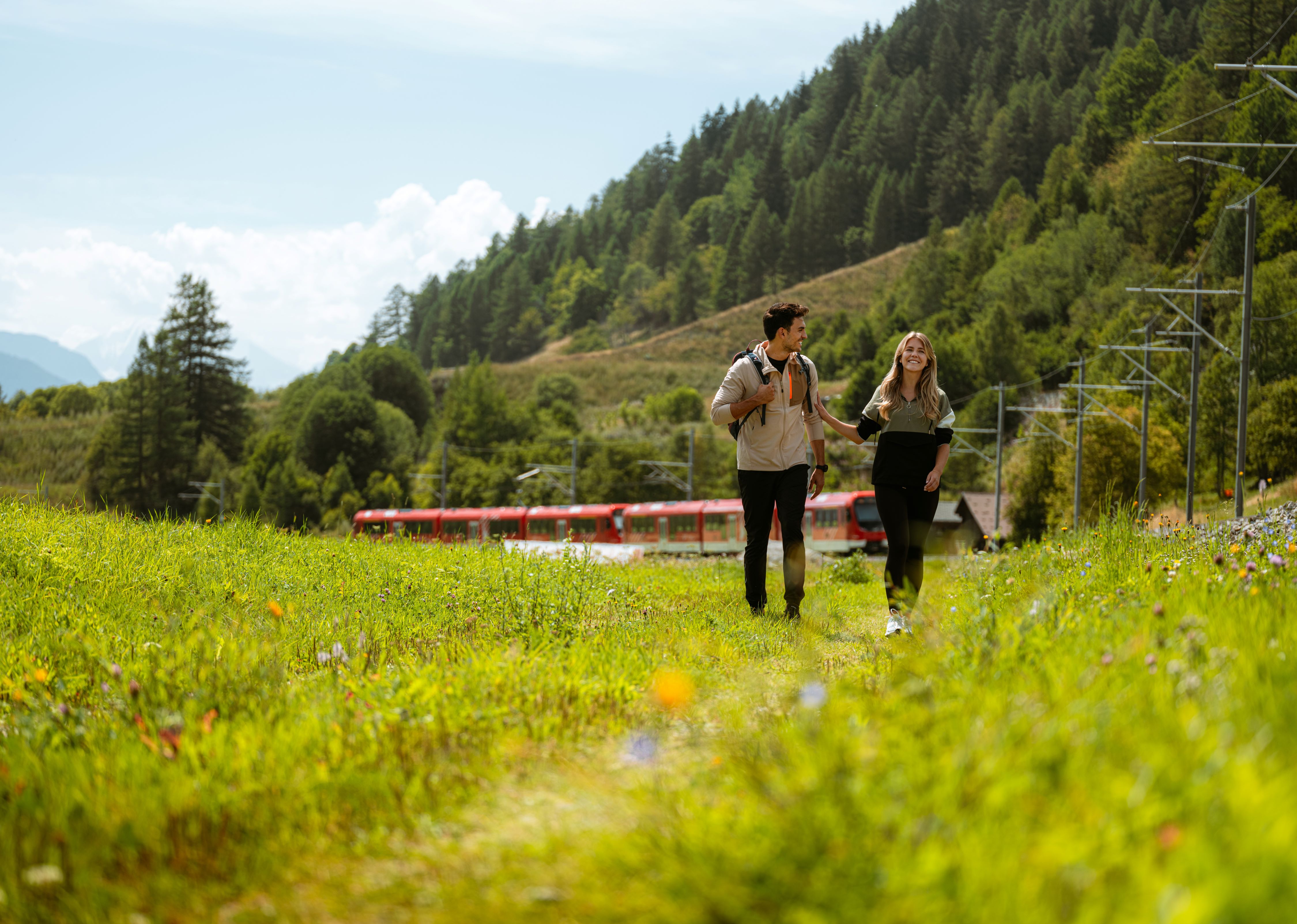 Ein Mann und eine Frau gehen an einem sonnigen Tag in der Region Goms wandern.