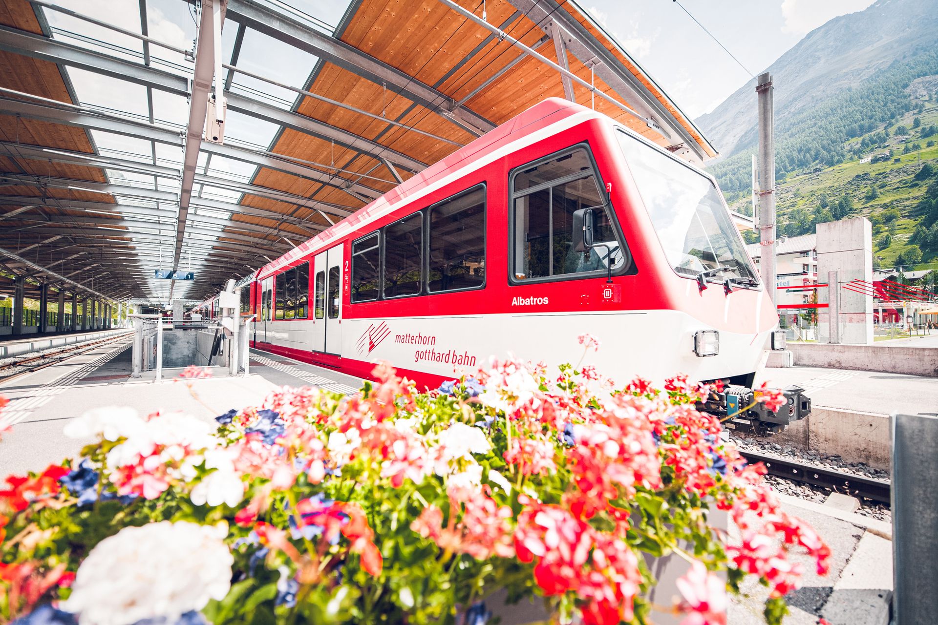 Bahnhof Matterhorn Terminal Täsch Abfahrt eines Zuges mit Blumen im Vordergrund