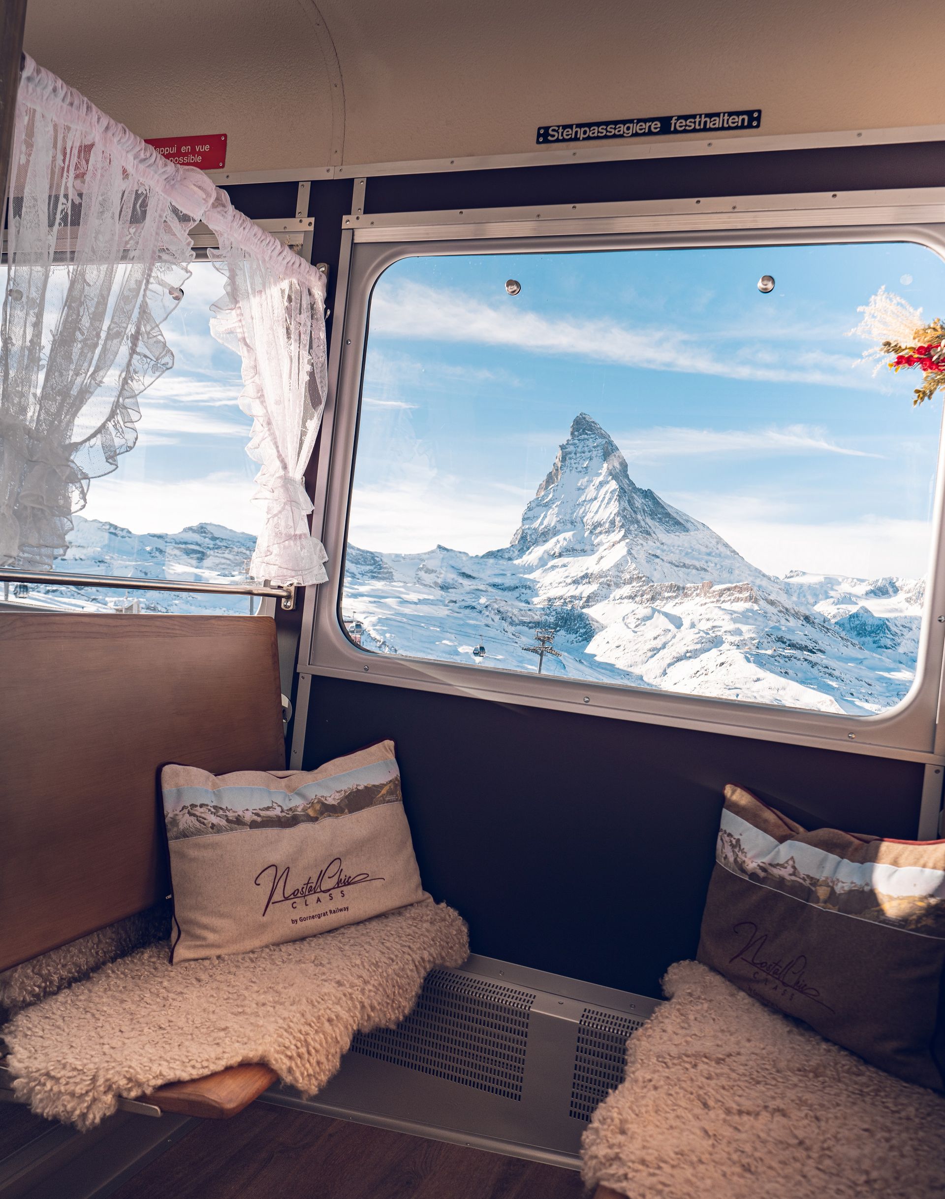 Der mit Kissen und Vorhängen geschmückte Waggon des NostalChic bietet eine gemütliche Atmosphäre. Aus dem Fenster zeigt sich das schneebedeckte Matterhorn unter einem blauen Himmel